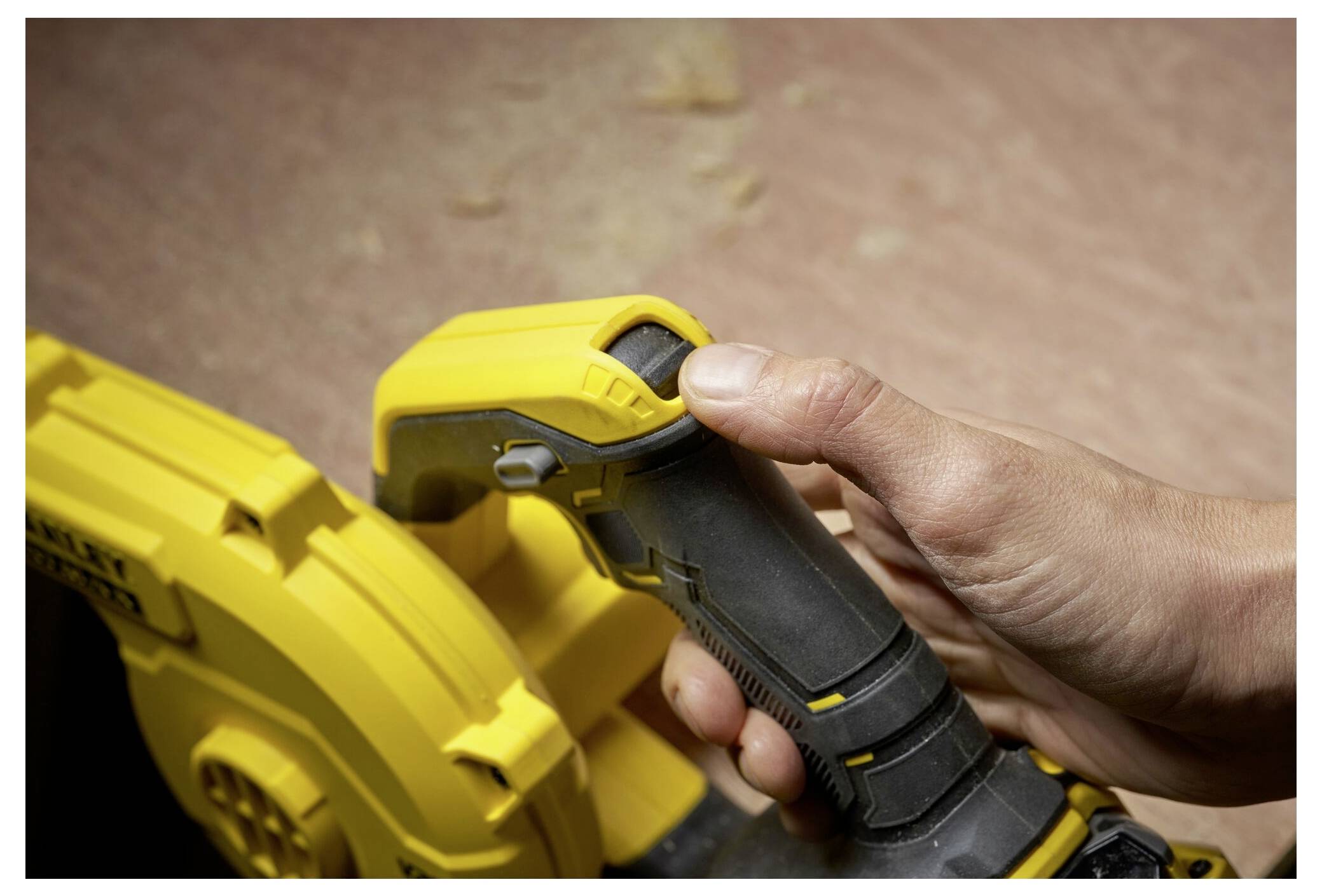Una persona afferra il manico di uno strumento elettrico giallo con una presa nera, preparandosi a utilizzarlo su uno sfondo di superficie in legno.