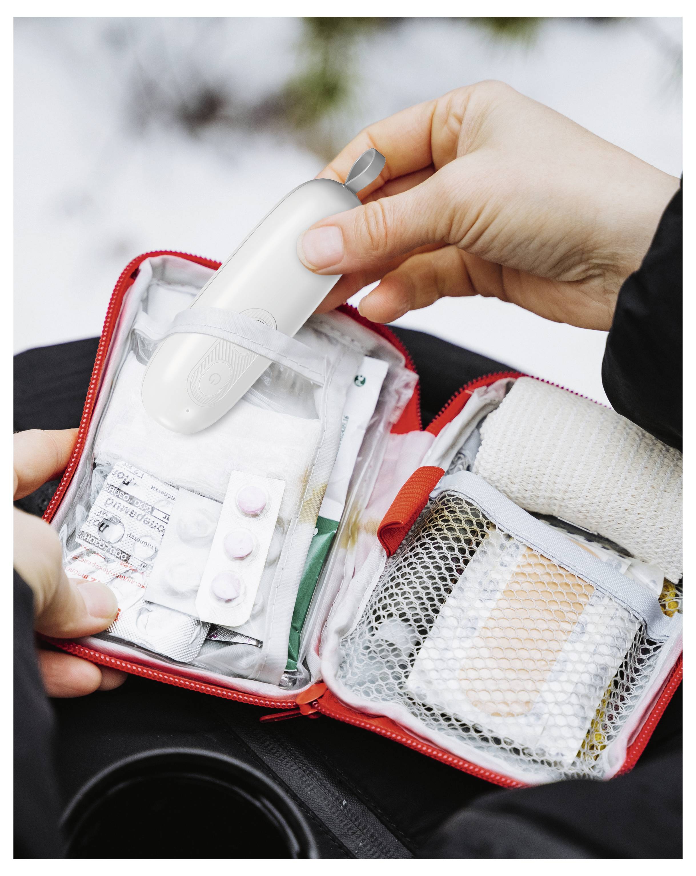 'Una persona apre un kit di pronto soccorso rosso contenente medicinali, garze e un dispositivo medico bianco, dimostrando preparazione per le emergenze.'