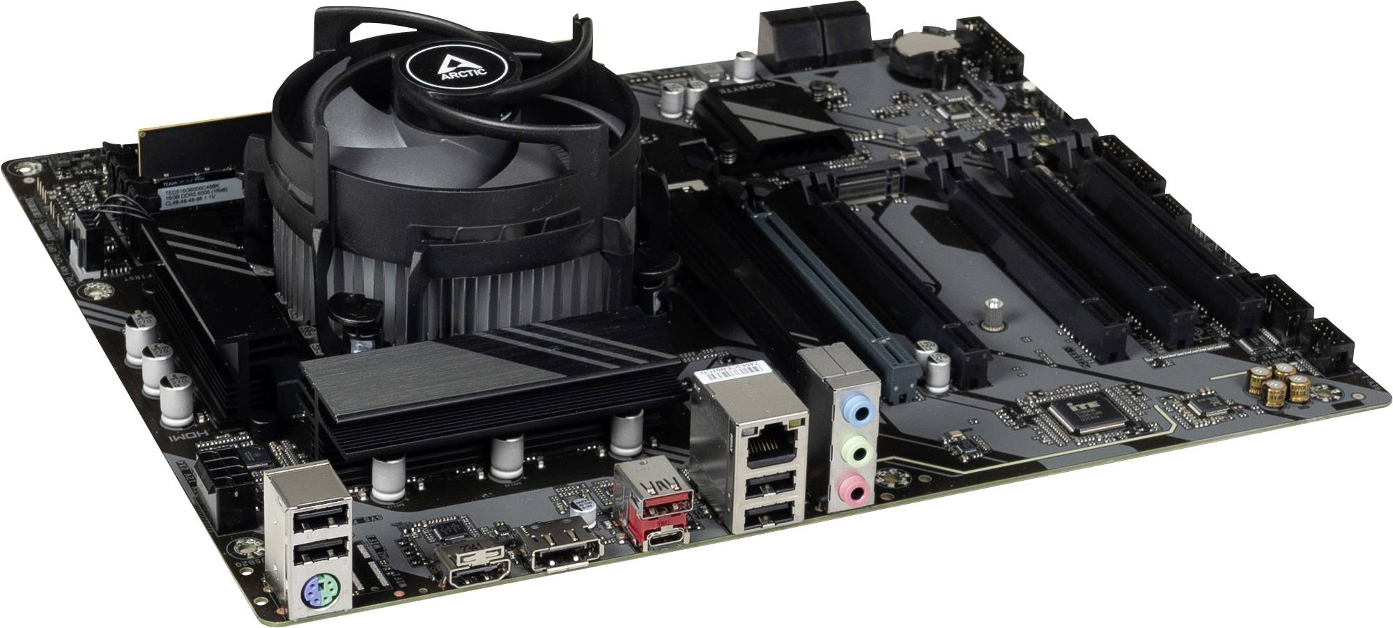 Scheda madre per computer desktop con ventola di raffreddamento della CPU installata e dissipatore di calore, che mostra le porte posteriori e gli slot di espansione su sfondo bianco.