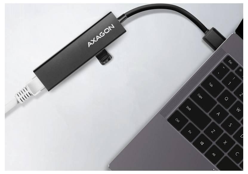 Adattatore USB AXAGON collegato a un laptop, con un cavo collegato che si estende dal dispositivo su una superficie bianca.