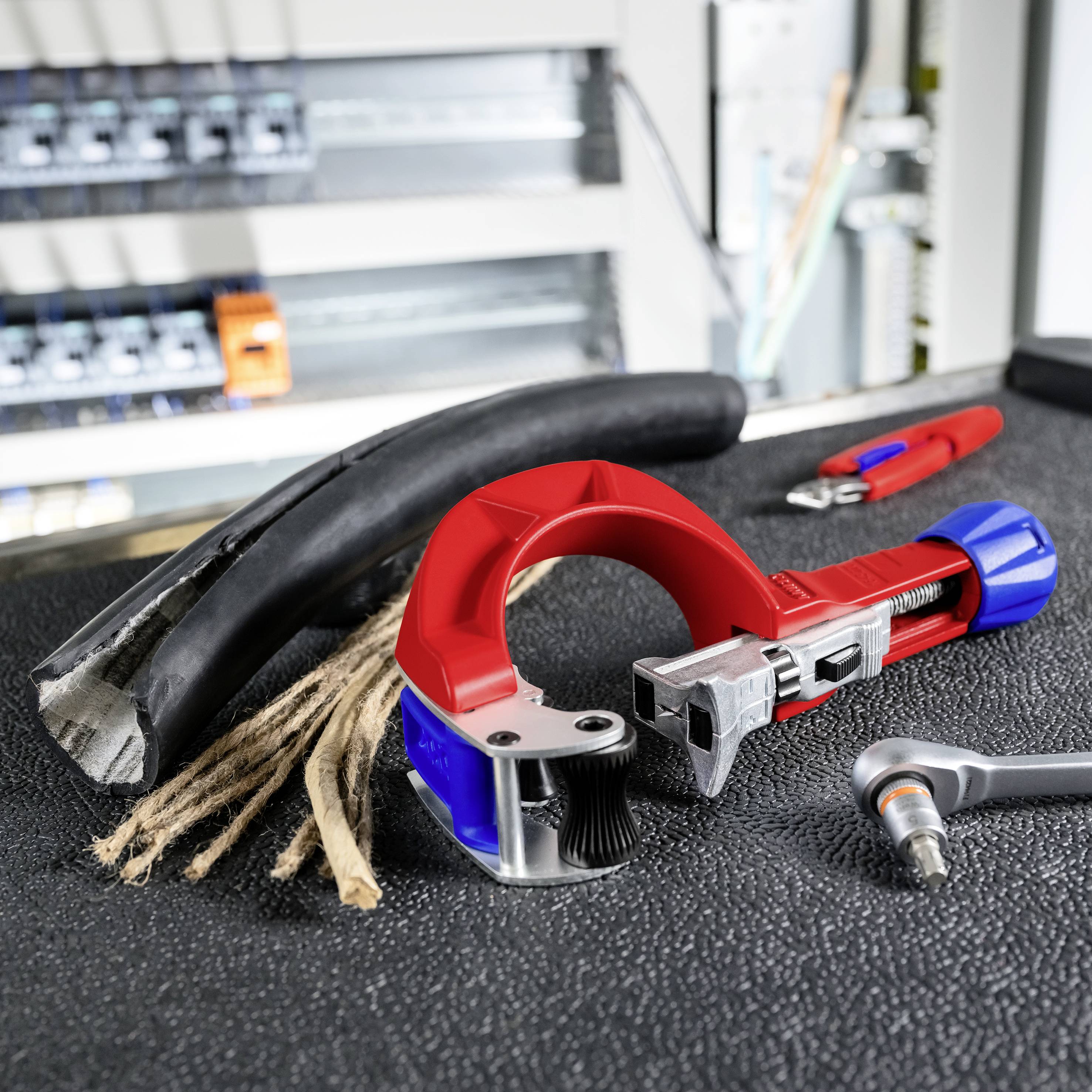 Strumenti per tagliare cavi e un cavo nero spellato posati su un banco da lavoro, con un tronchese rosso e blu e uno spelafili in un'officina.