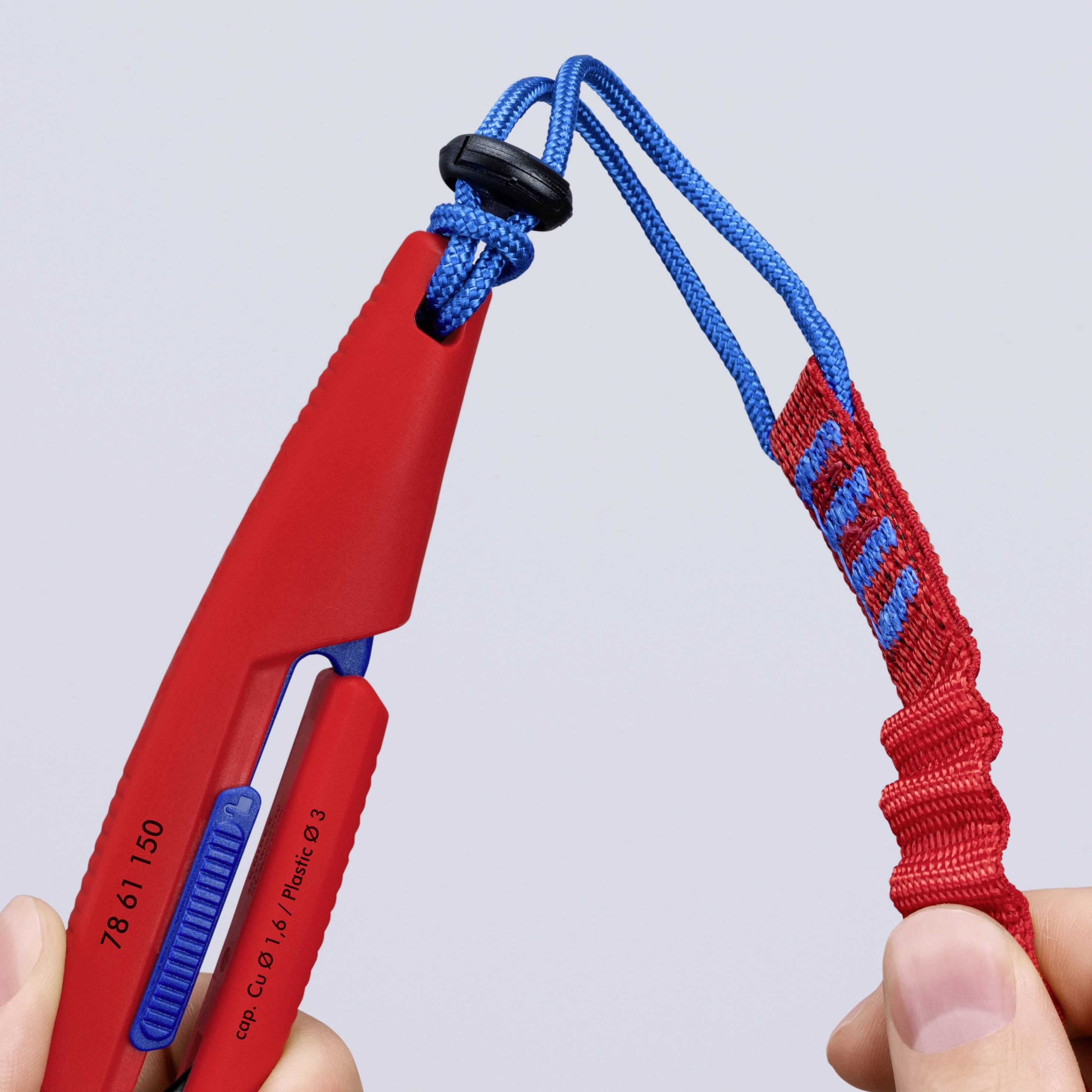 Primo piano di un dispositivo di assicurazione per arrampicata rosso e blu con una corda infilata attraverso di esso, tenuto in mano su uno sfondo neutro.