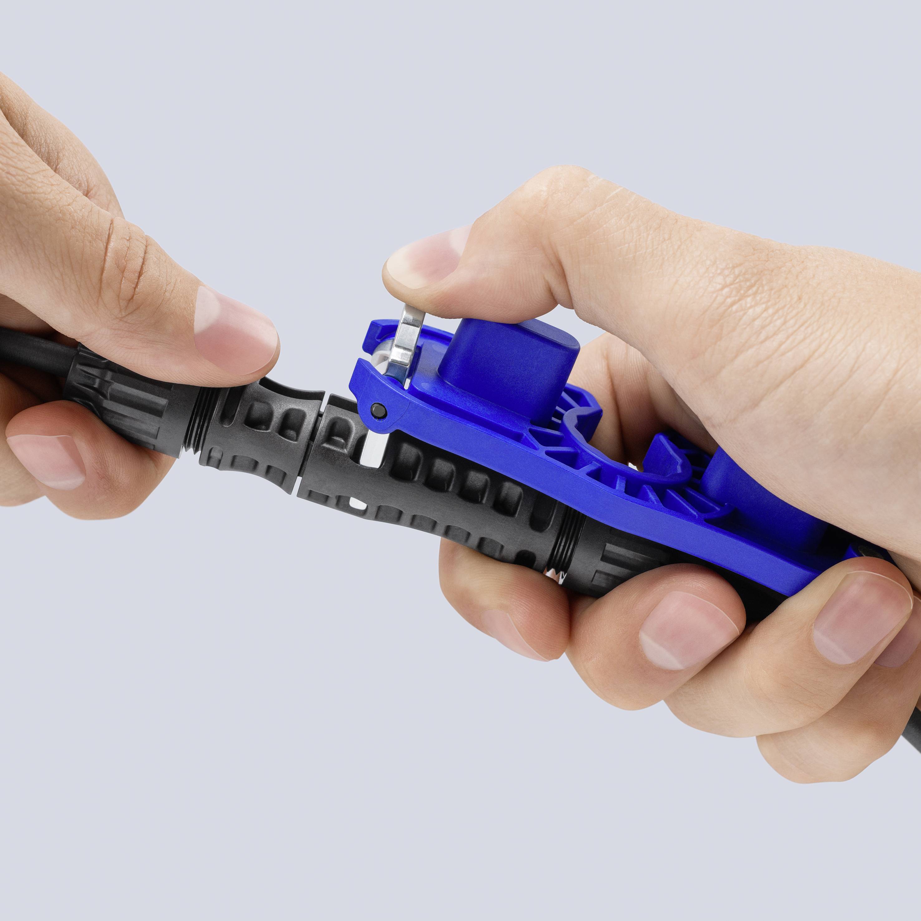 Le mani utilizzano uno strumento blu per spellare i cavi per tagliare la guaina esterna di un cavo nero.