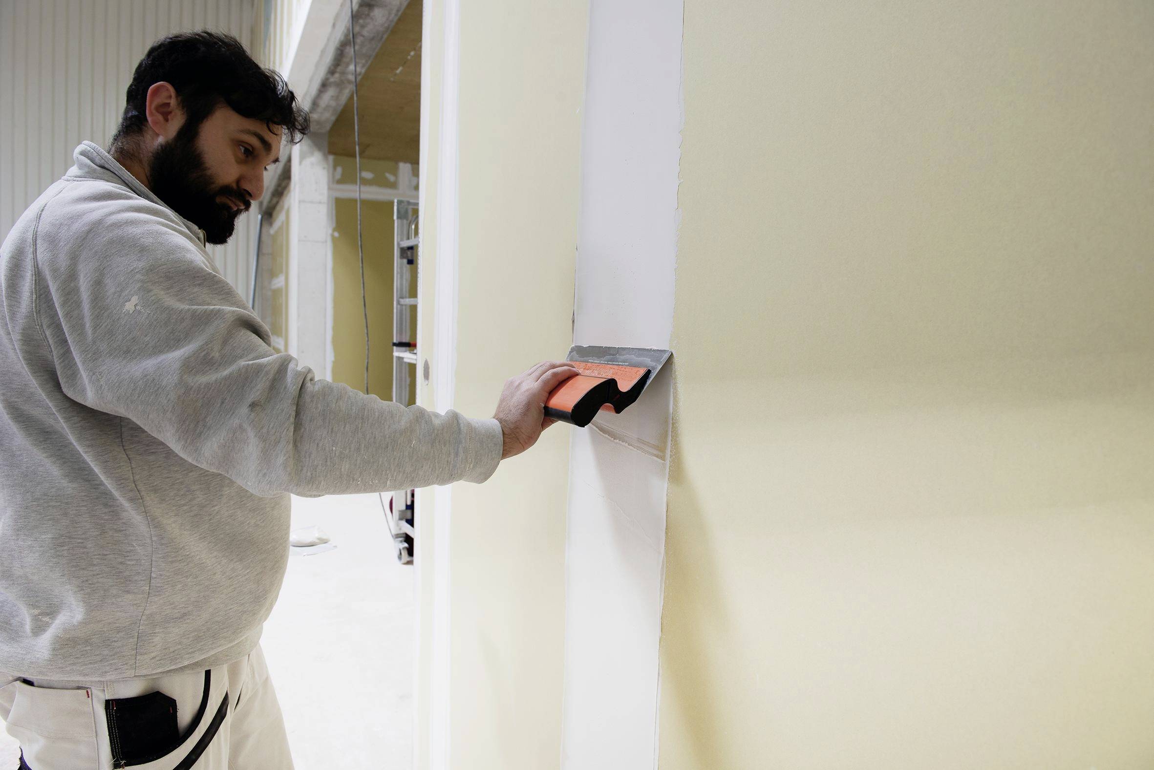 Un uomo che stende lo stucco per giunti su una giuntura di parete con una spatola durante la finitura interna del cartongesso.