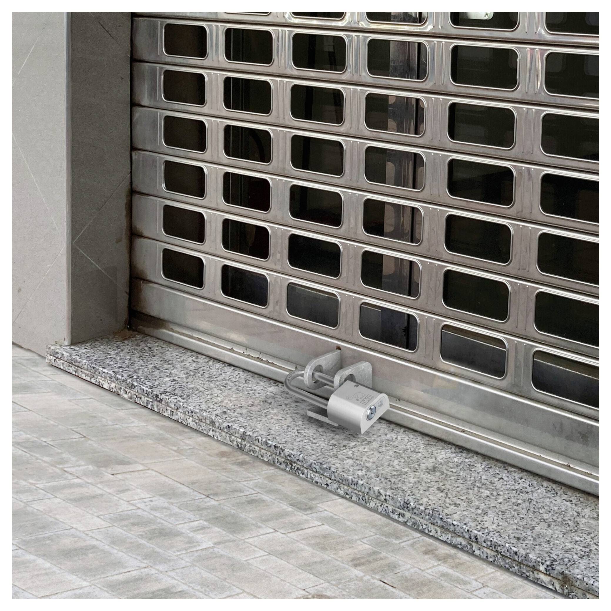 Persiana di sicurezza in metallo chiusa bloccata con un lucchetto in basso, che ostruisce l'ingresso di un negozio.