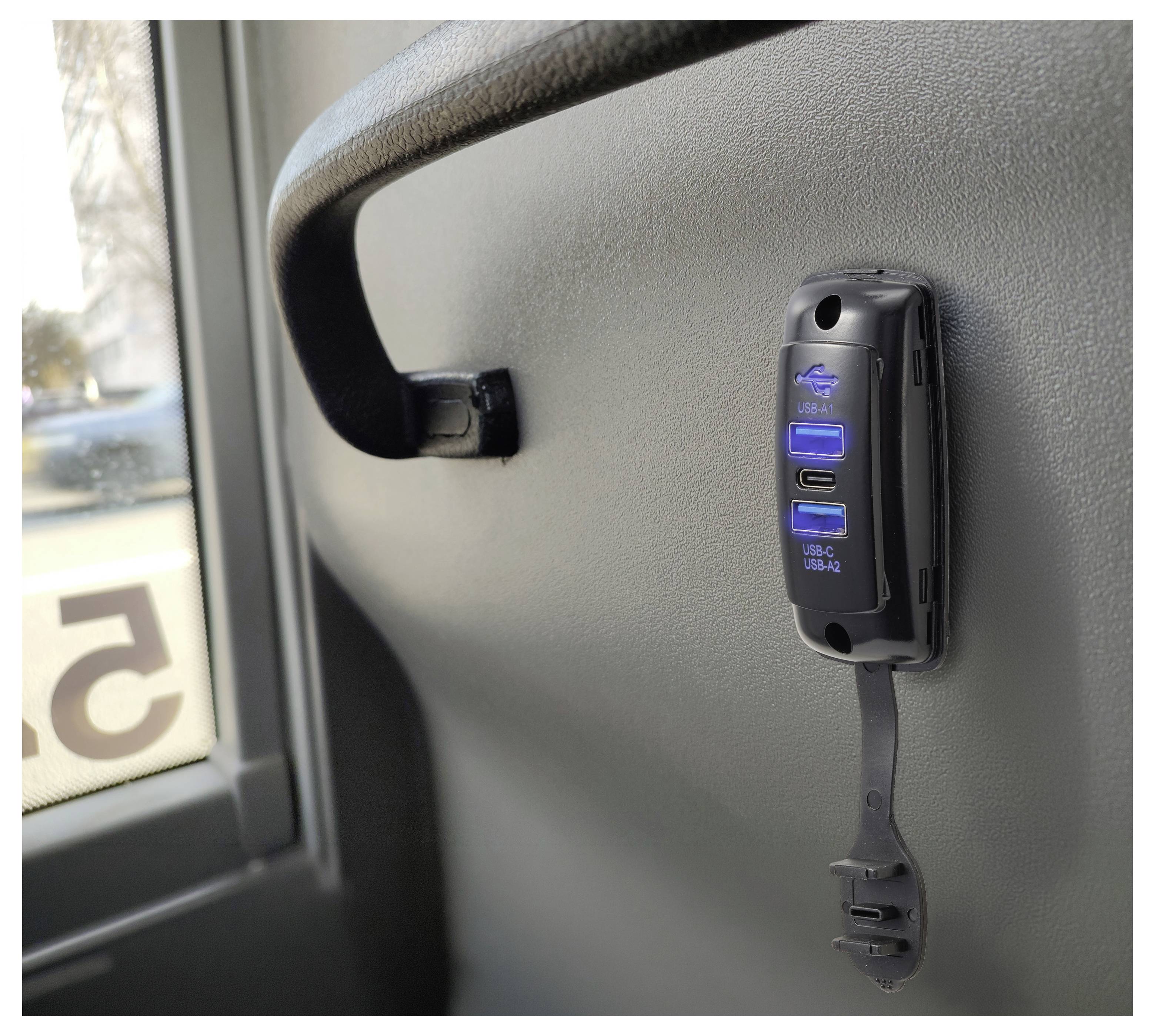 Un poggiatesta di autobus con un adattatore di alimentazione USB montato e un cavo di ricarica, accanto a una finestra.