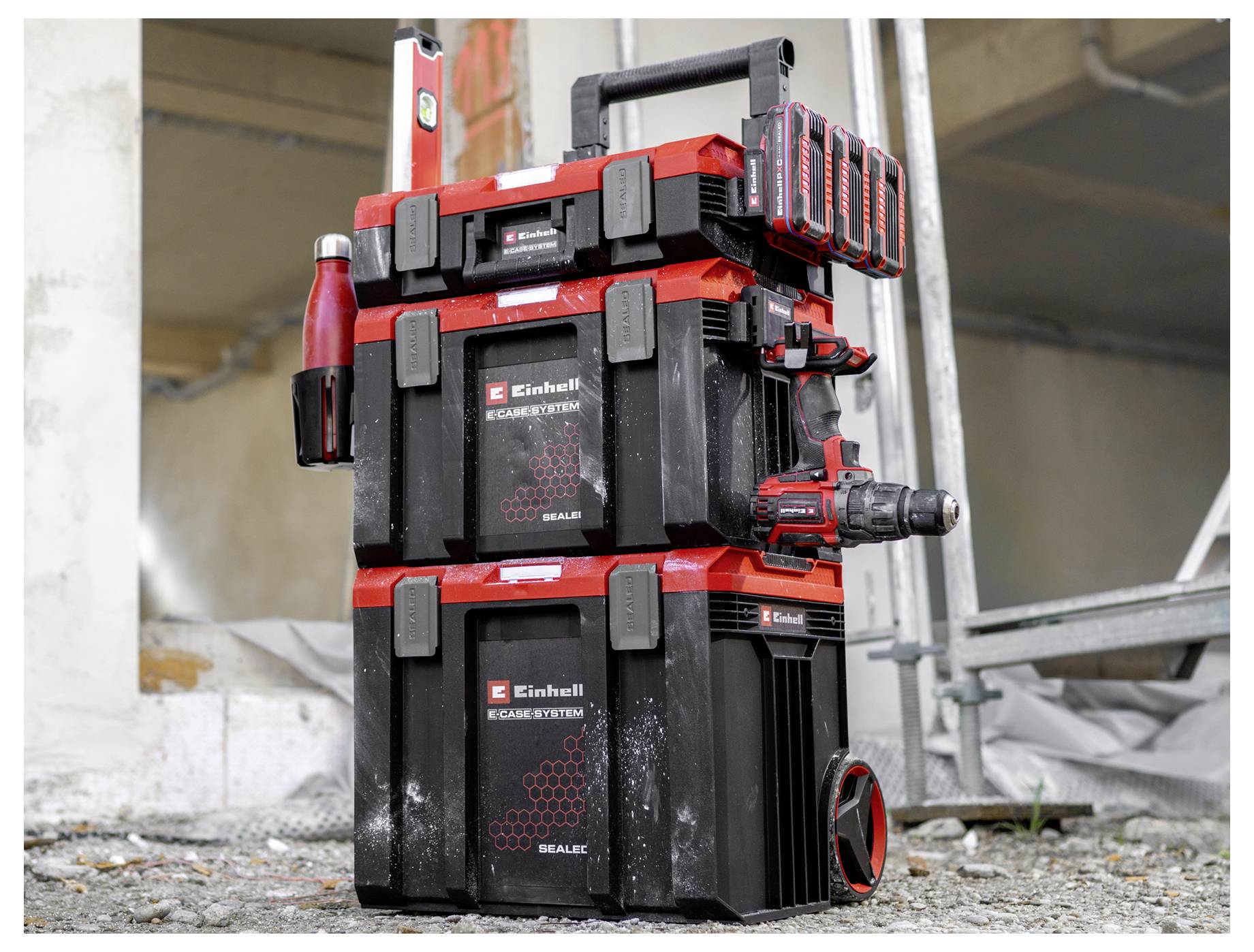 Cassette di conservazione Einhell rosso e nero stacked in un cantiere edile, con maniglia, bottiglie e accessori montati.