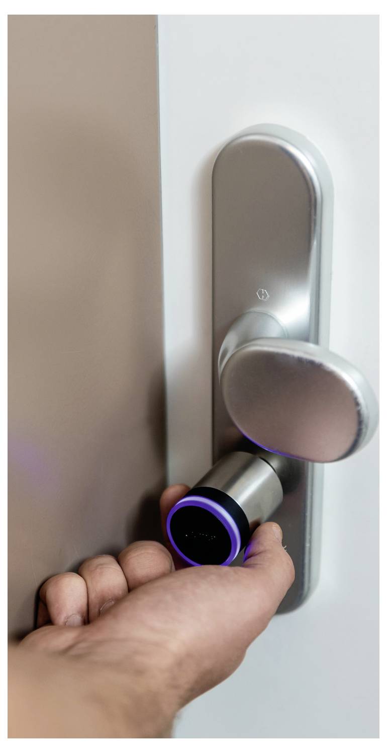 La mano apre una porta moderna con maniglia rotonda e serratura elettronica.