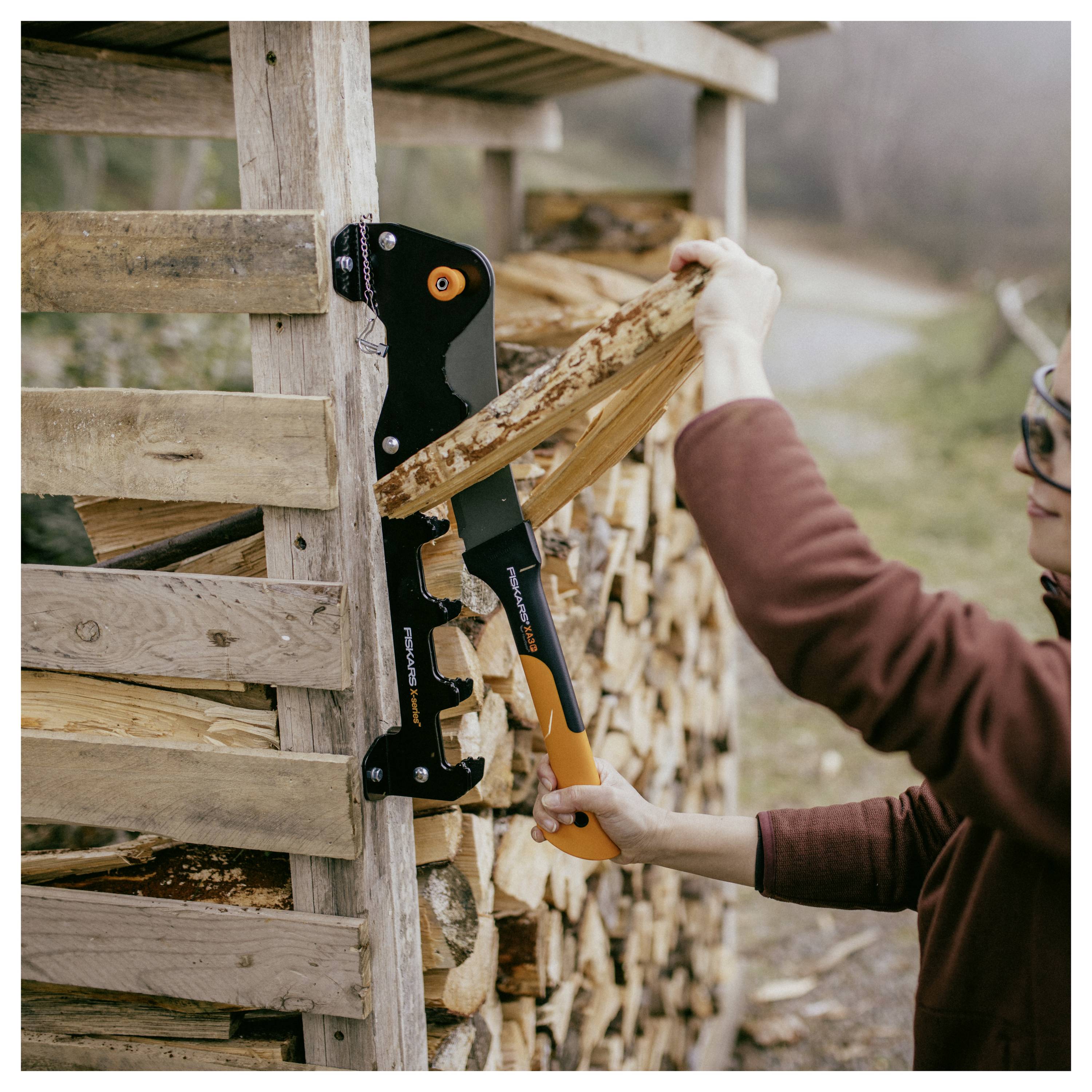 Persona che utilizza un'ascinatrice manuale per spaccare legna da ardere impilata accanto a una capanna di legno all'aperto.