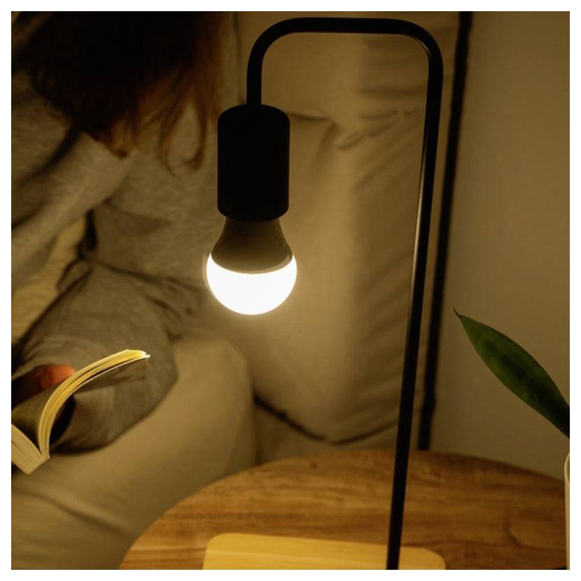 Una persona legge un libro alla luce di una piccola lampada luminosa su un comodino in una stanza accogliente e debolmente illuminata.
