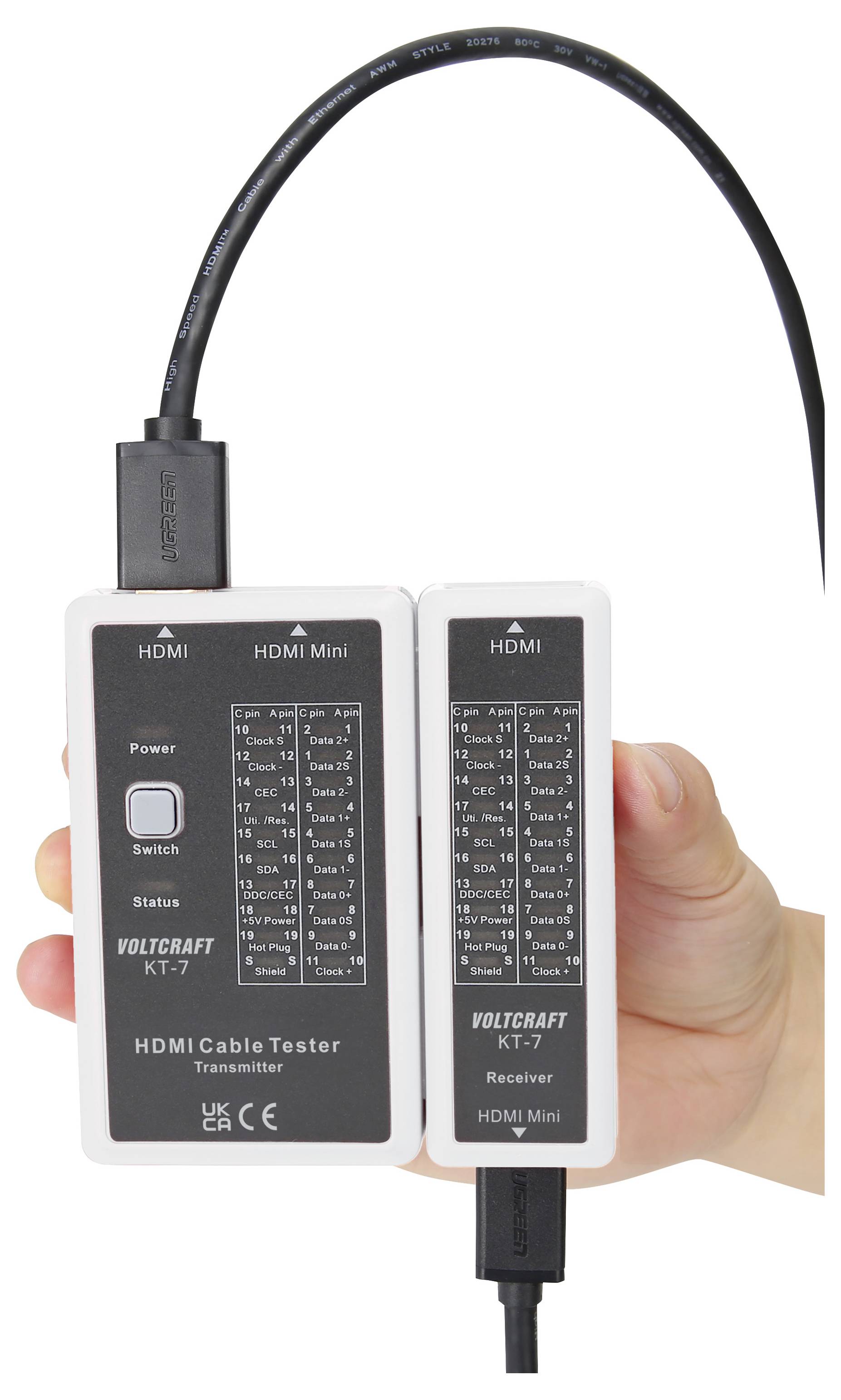 Mano che tiene un tester per cavi HDMI Voltcraft KT-7 con trasmettitore e ricevitore collegati da un cavo, che mostra porte etichettate e indicatori di stato.