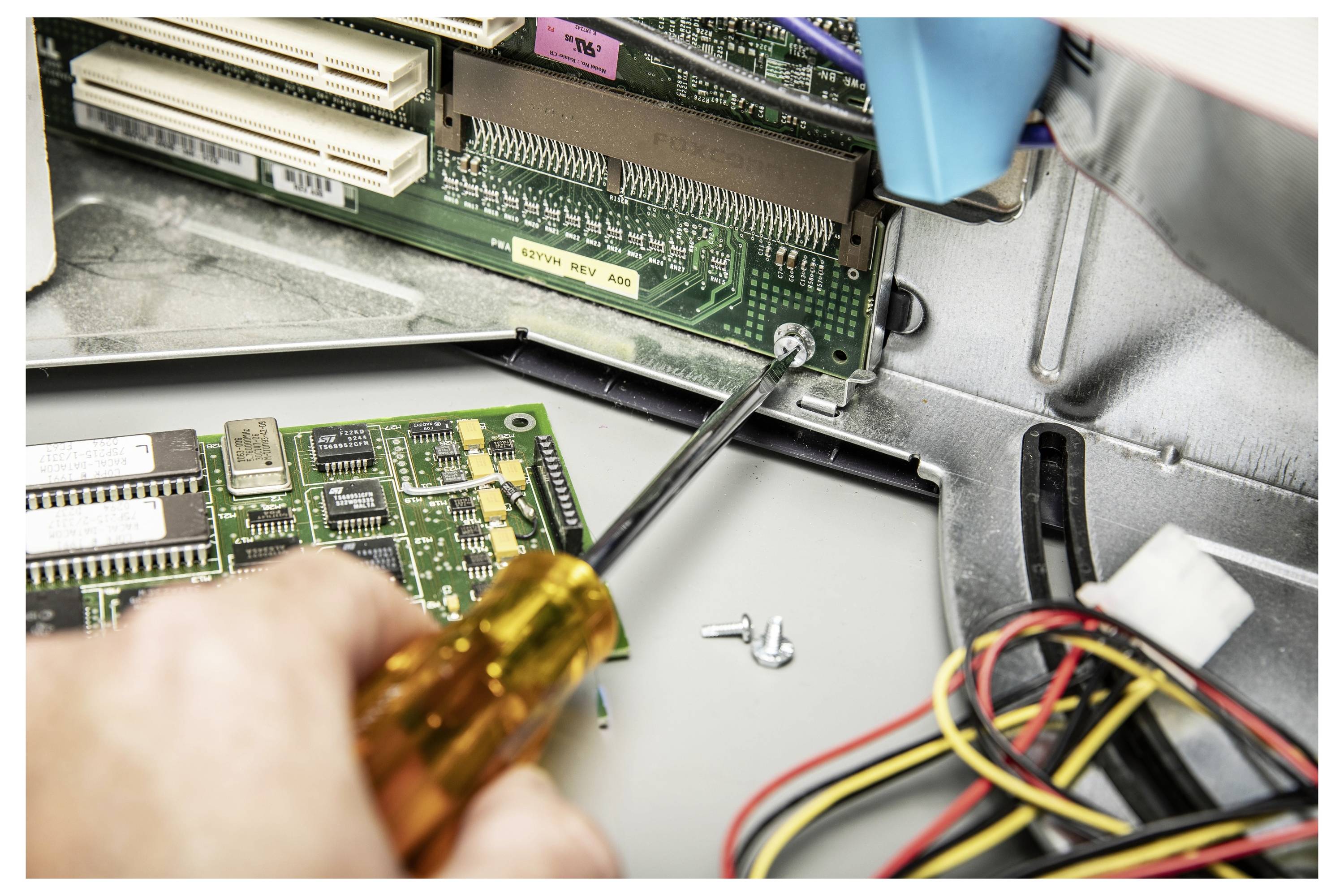 Primo piano di un cacciavite che rimuove una vite da una scheda a circuiti all'interno di un dispositivo elettronico, con fili e componenti sciolti nelle vicinanze.