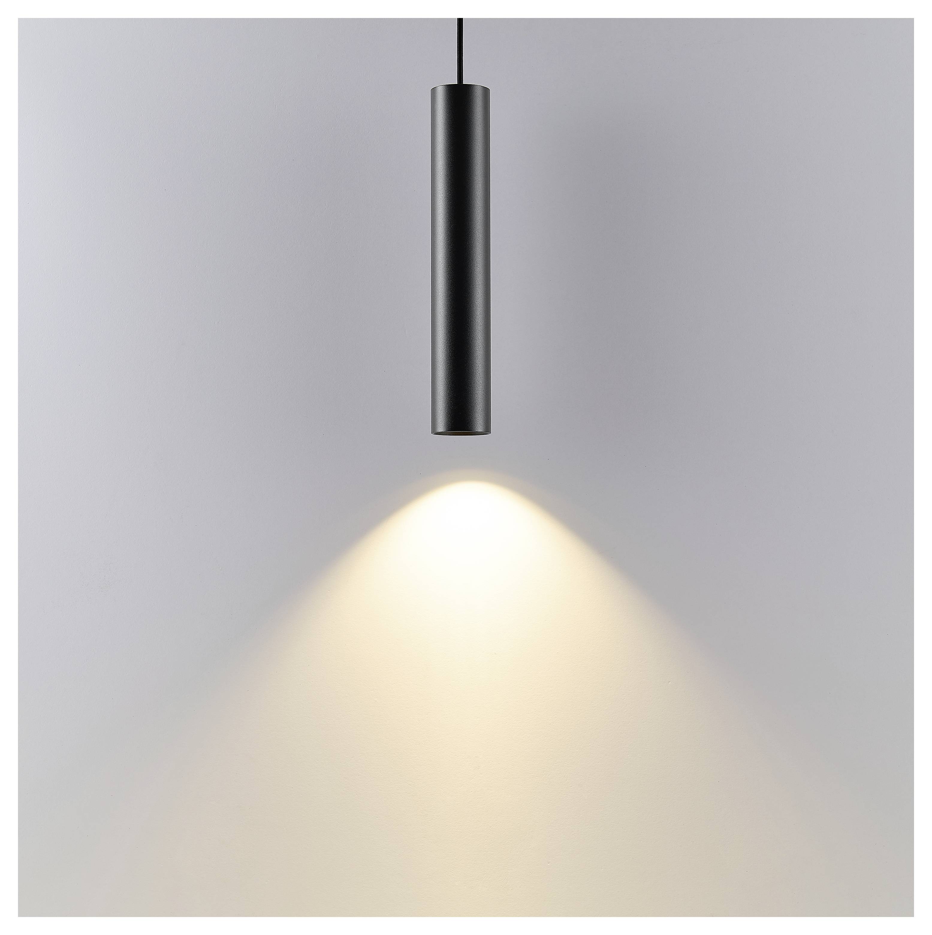 Luce a sospensione cilindrica nera che pende dal soffitto, proiettando un caldo cono di luce su un muro grigio semplice.