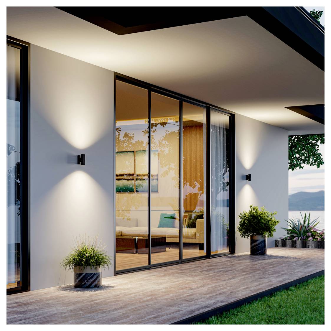 Patio di una casa moderna con grandi porte scorrevoli in vetro che si aprono su un soggiorno arredato, illuminato da applique murali e delimitato da piante in vaso e prato.
