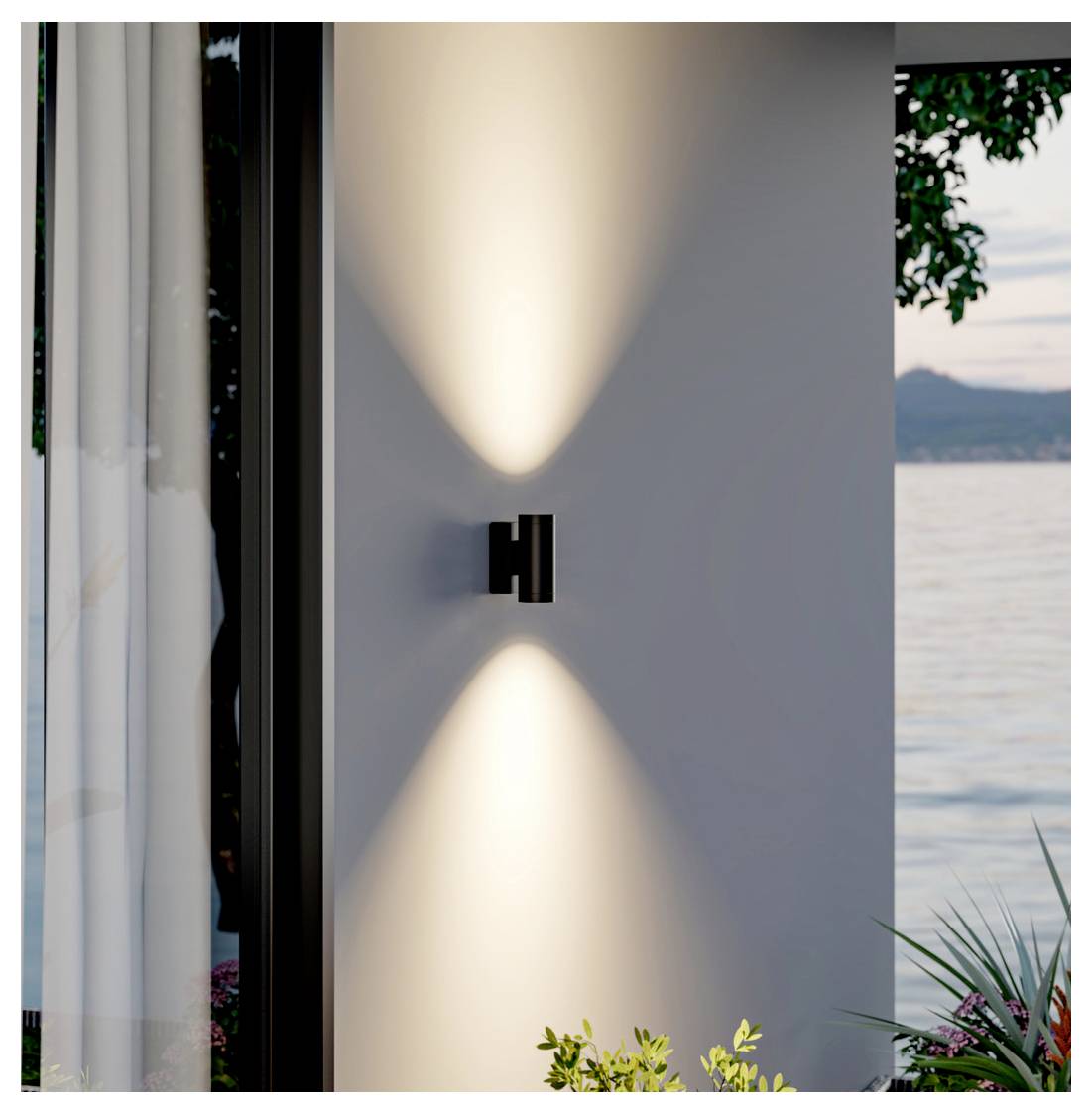 Applique murale moderna che proietta fasci di luce calda simmetrica su una parete esterna bianca accanto a una finestra, con vista lago e piante nelle vicinanze.