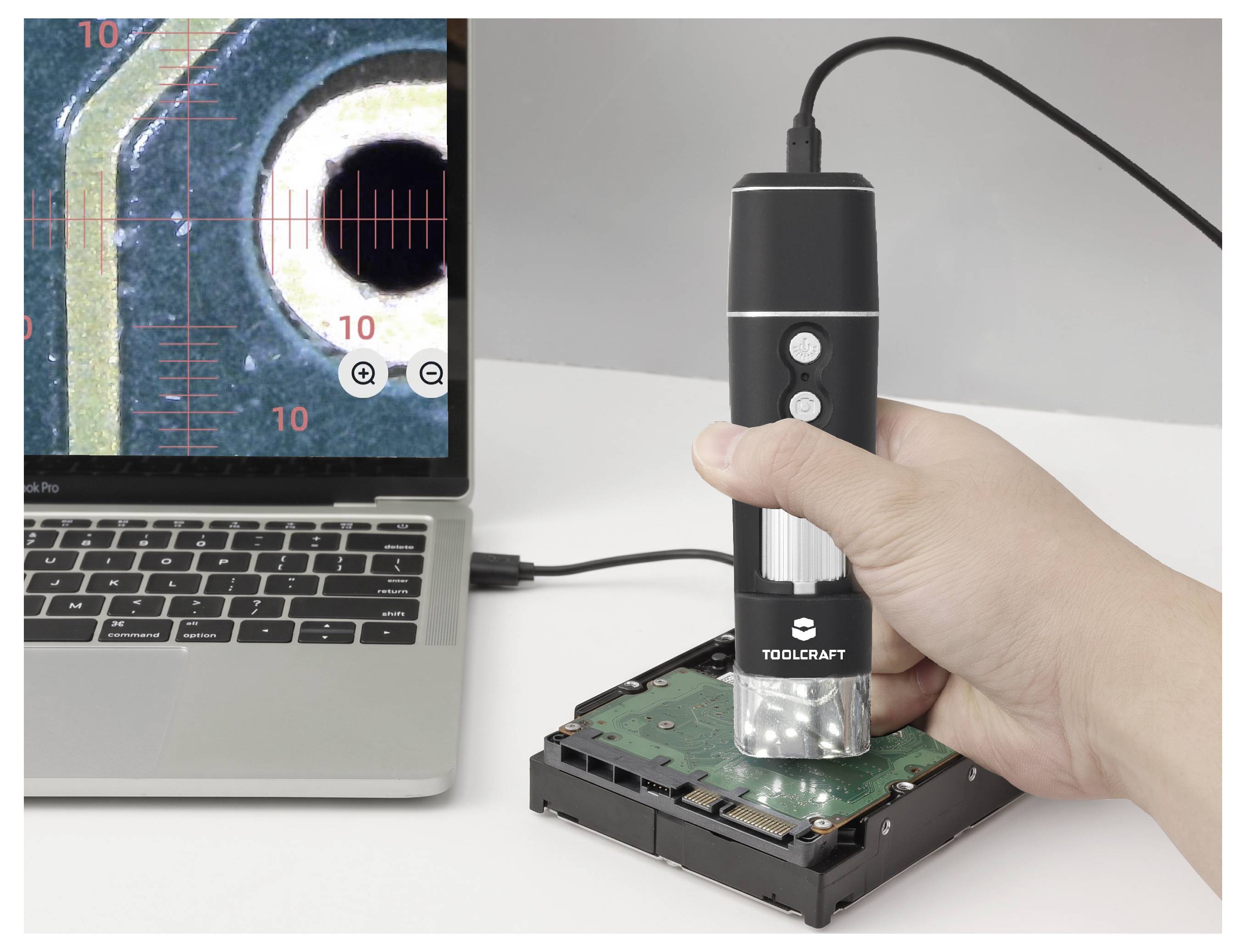 Microscopio digitale portatile che ispeziona un circuito stampato del disco rigido accanto a un laptop che visualizza una vista ingrandita.