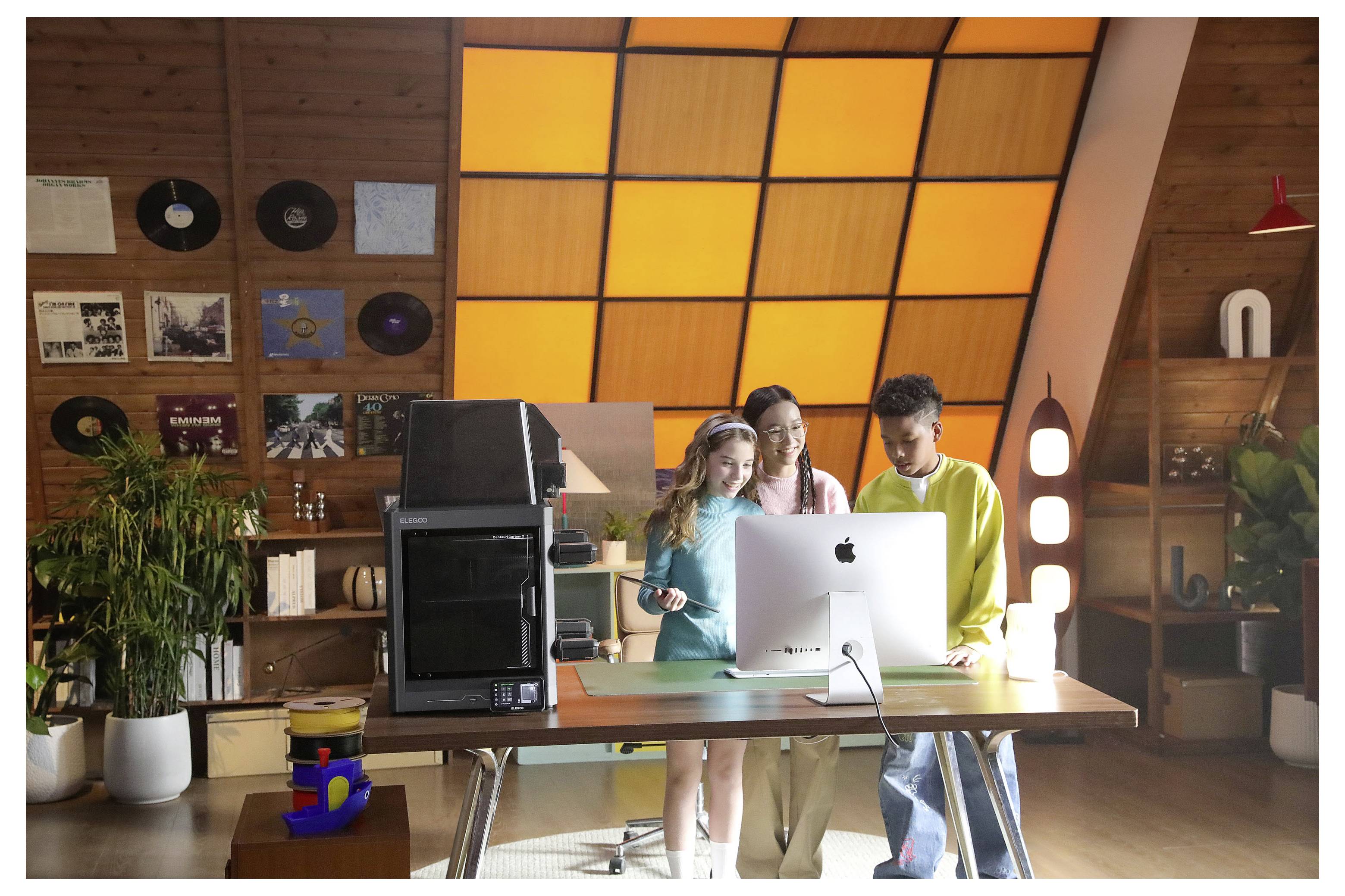 Tre persone collaborano intorno a un iMac in un ufficio caldo con pareti in legno e una parete di finestre che brilla di un'arancione luminoso.