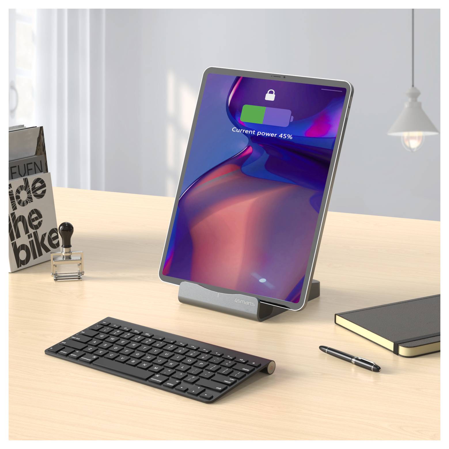 Tablet su un scrivania in un supporto che mostra una schermata bloccata con "Potenza attuale 45%", accanto a una tastiera, un quaderno e una penna.