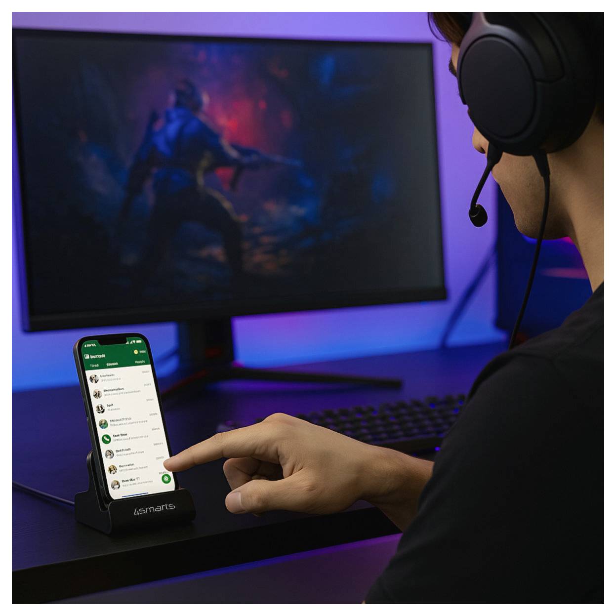 Una persona che indossa un auricolare punta a uno smartphone su un dock da scrivania accanto a un monitor da gaming, suggerendo un uso di gaming o app.