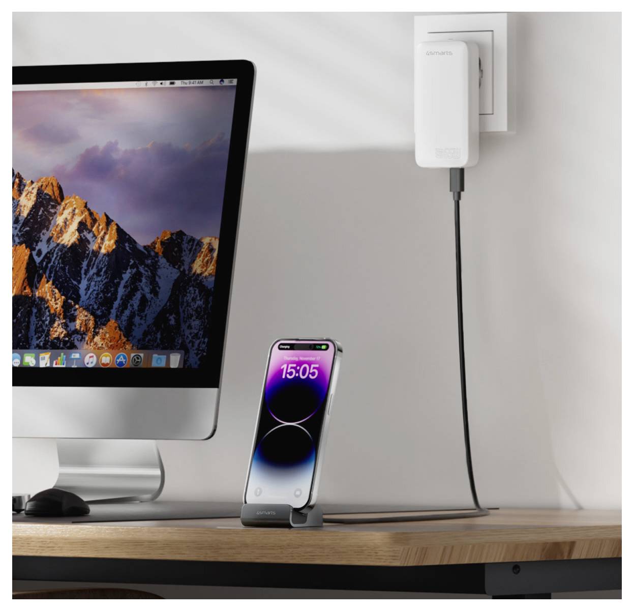 Setup desktop con un iMac e un iPhone su un supporto in carica da un adattatore da parete, con un cavo che corre verso la scrivania.