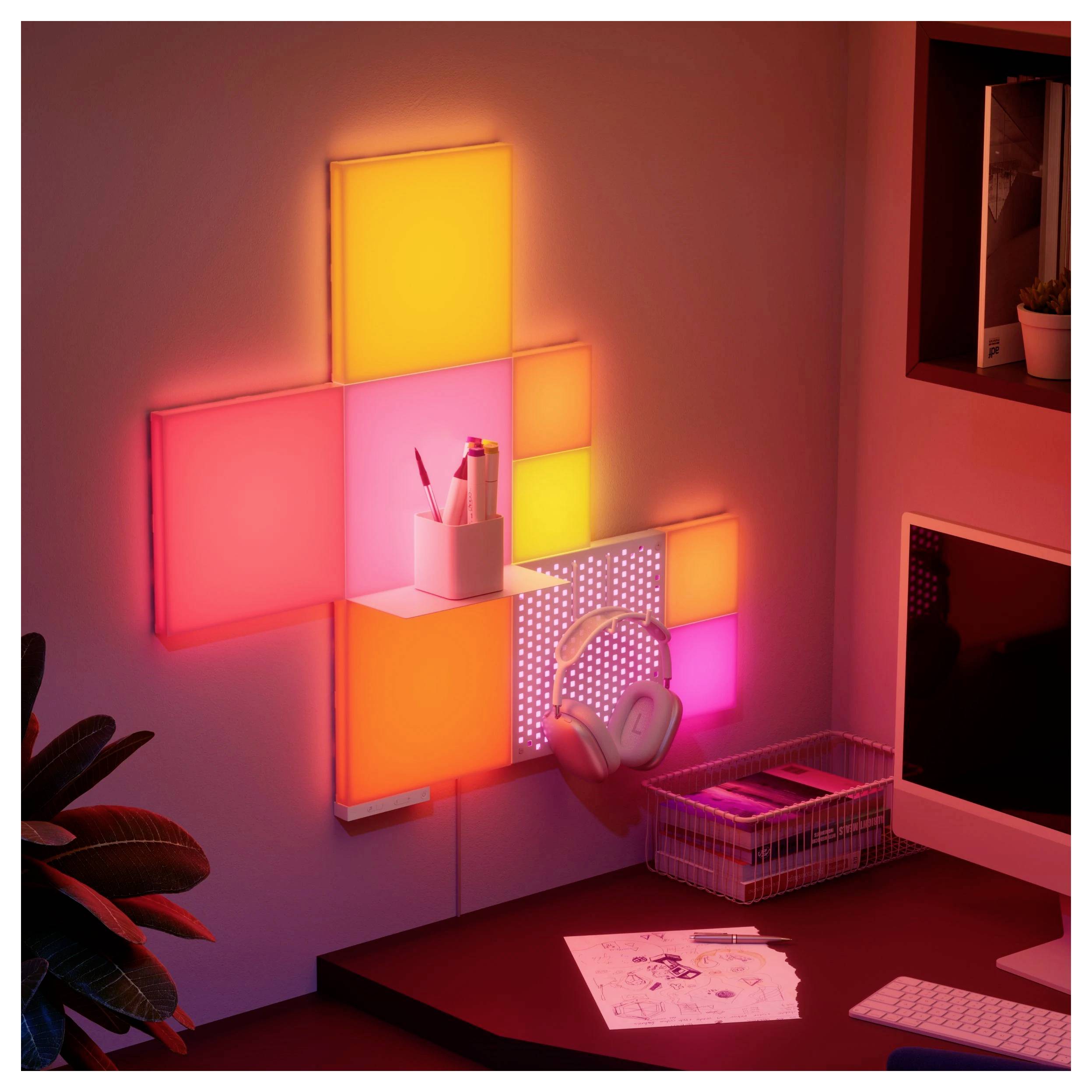Luci geometriche colorate sulla parete illuminano un'area di lavoro con un portapenne, cuffie, fogli, una tastiera e un monitor in uno spazio di lavoro moderno.
