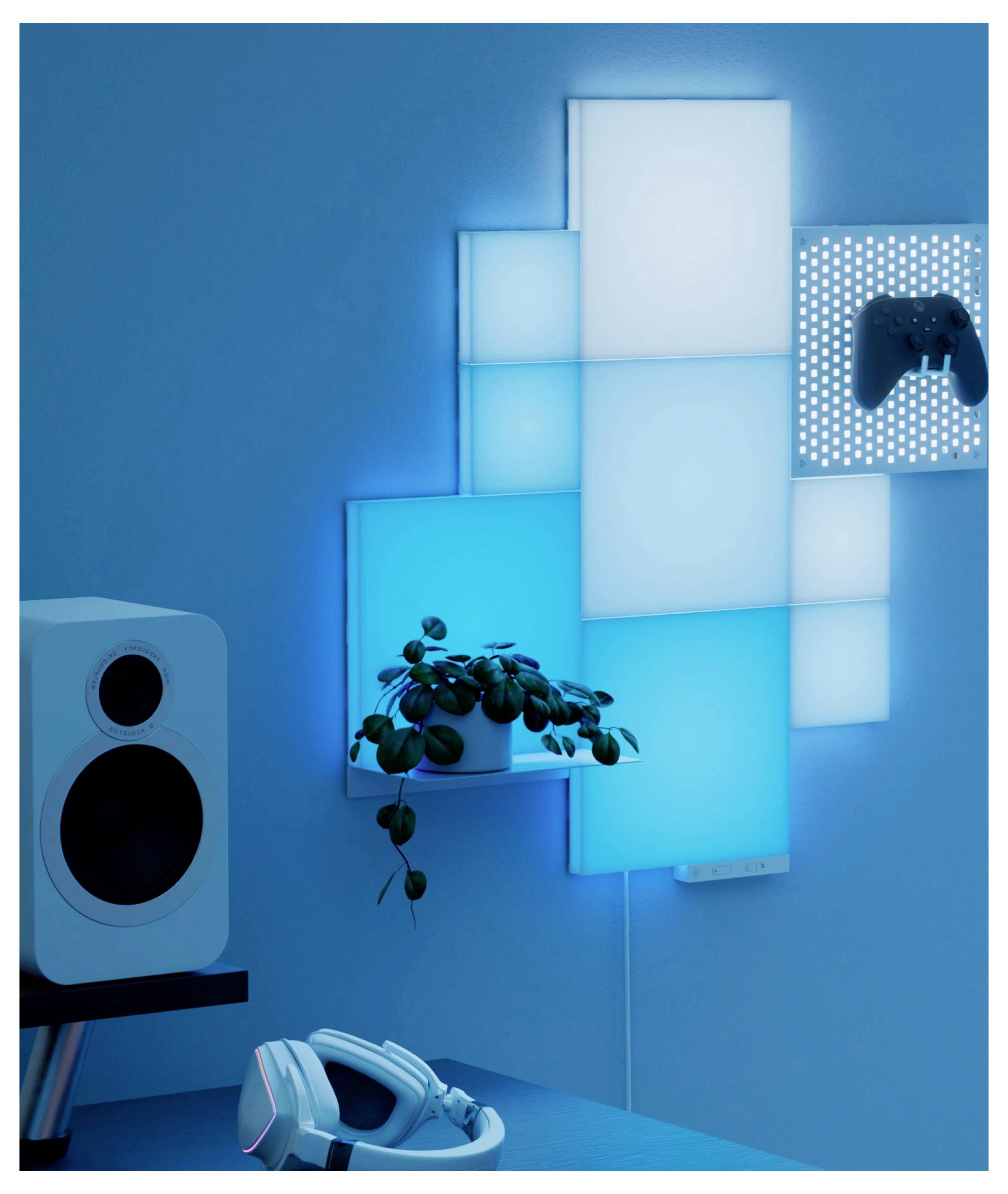 Stanza da gioco illuminata di blu con pannelli luminosi quadrati montati a parete, un controller per giochi su un pannello forato, altoparlanti e un visore VR sulla scrivania.