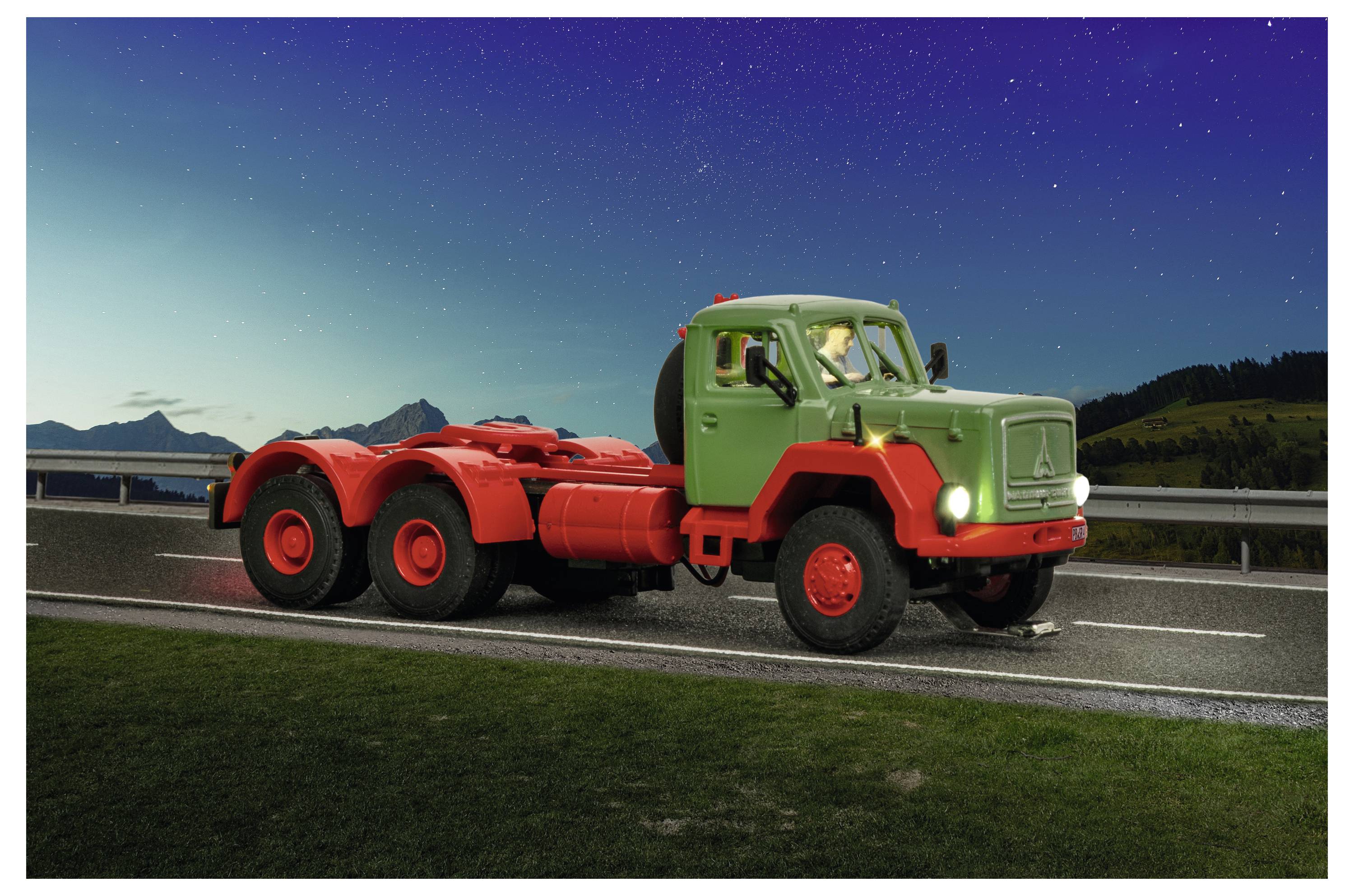 Un colorato camion vintage a sei ruote è parcheggiato a bordo strada al tramonto, con la cabina verde, il telaio rosso e le montagne sullo sfondo.