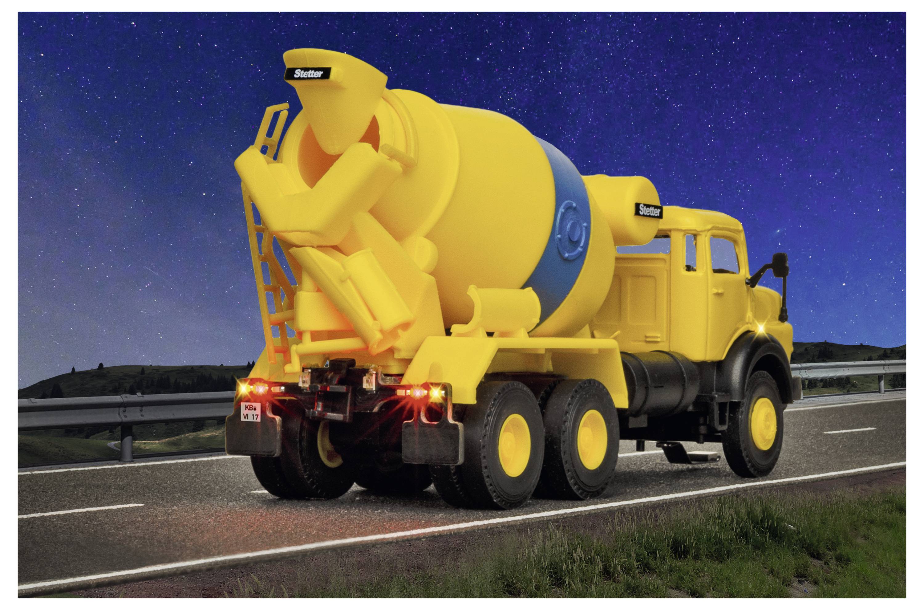 Camion betoniera giallo che guida su un'autostrada di notte sotto un cielo stellato, visto dal lato posteriore.