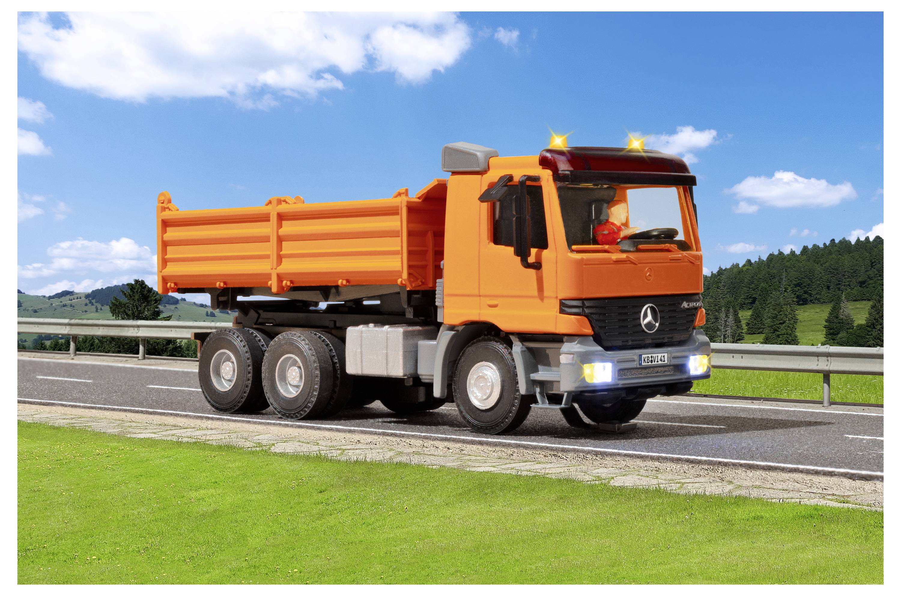 Camion ribaltabile arancione parcheggiato sulla spalla di un'autostrada accanto all'erba verde e alle sponde di protezione sotto un cielo blu.