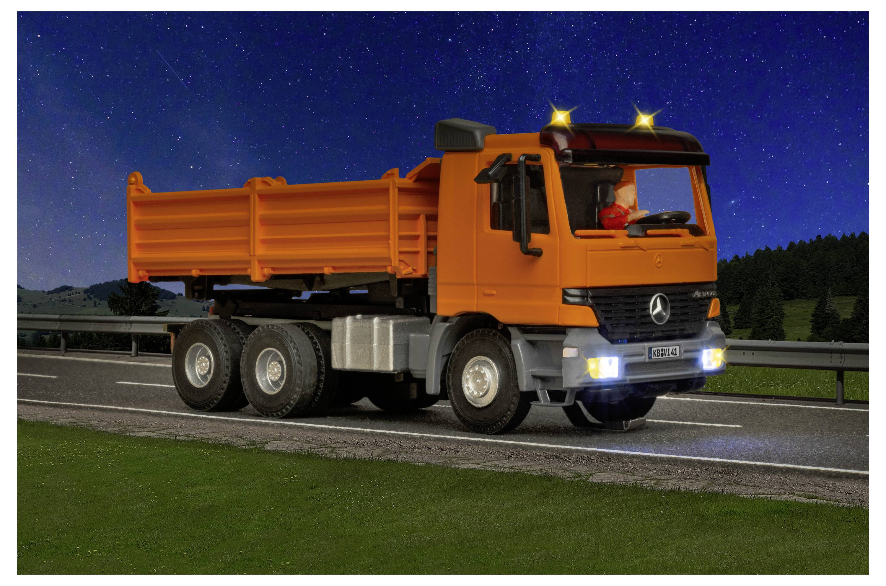 Camion ribaltabile arancione che guida su un'autostrada di notte con i fari accesi e un cielo stellato sullo sfondo.