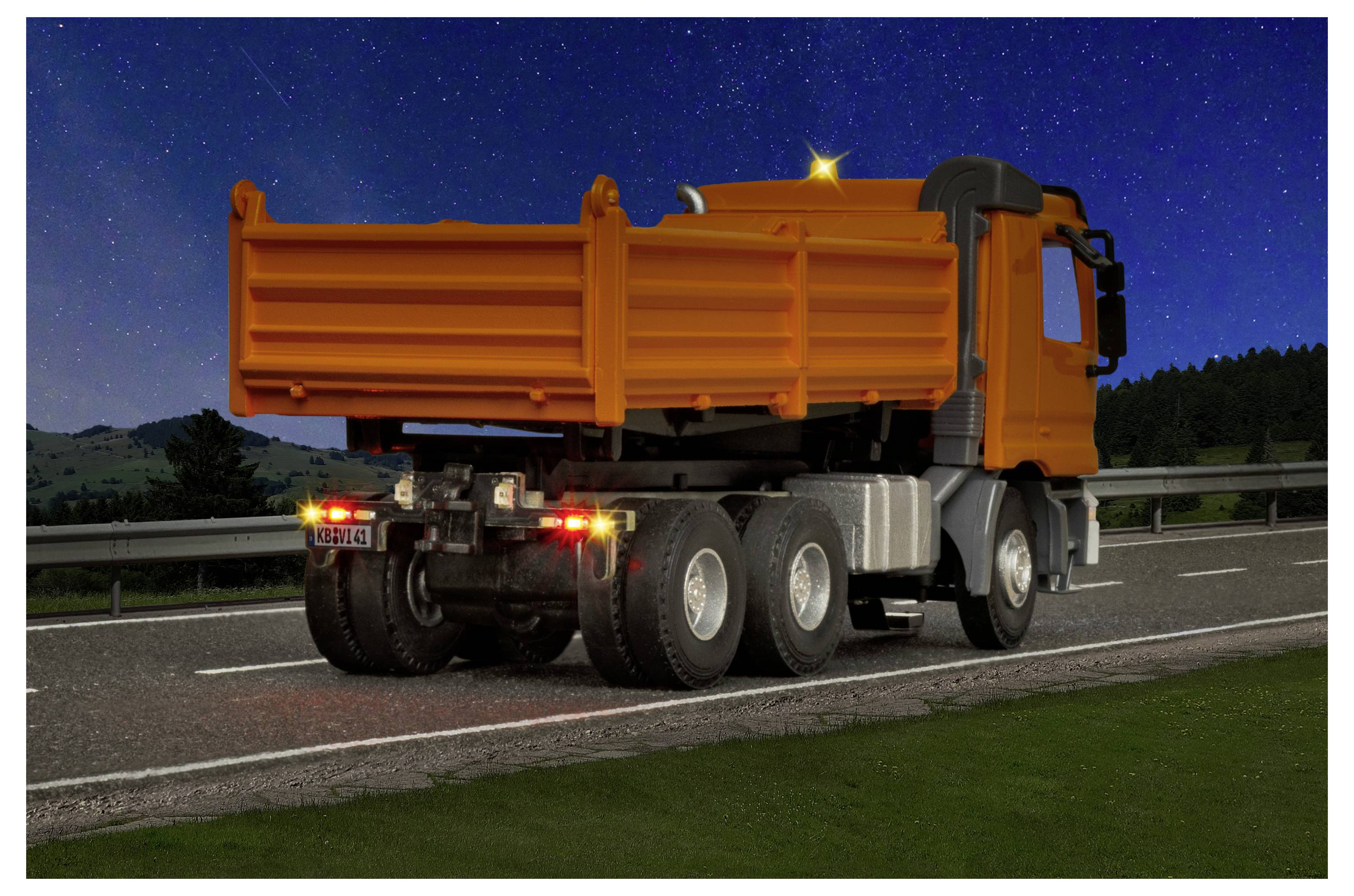 Camion ribaltabile arancione parcheggiato al margine della strada di notte, le luci posteriori che brillano sotto un cielo stellato.