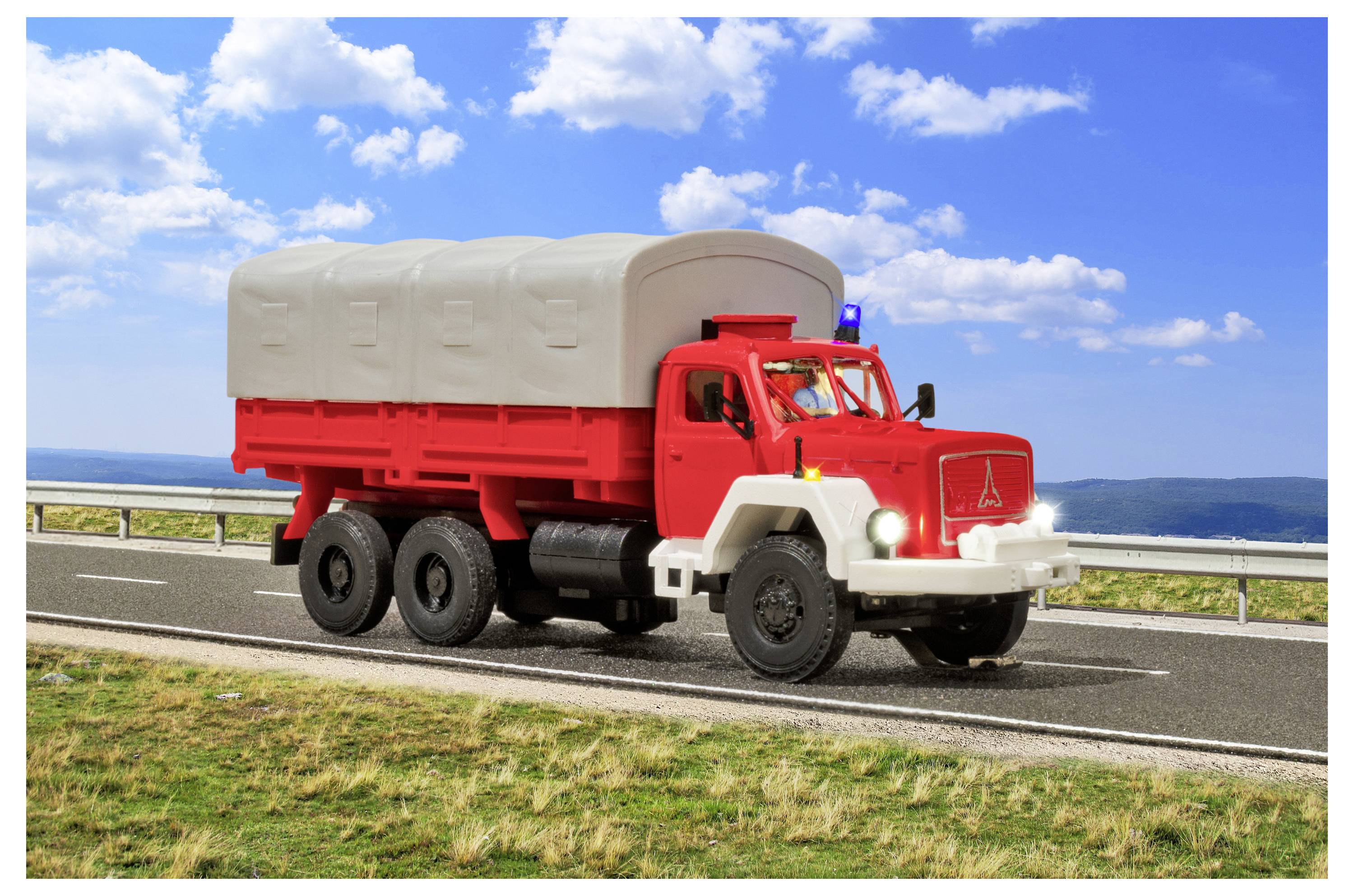 Camion rosso e bianco a sei ruote che trasporta merci che guida su una strada costiera sotto un cielo blu con nuvole.