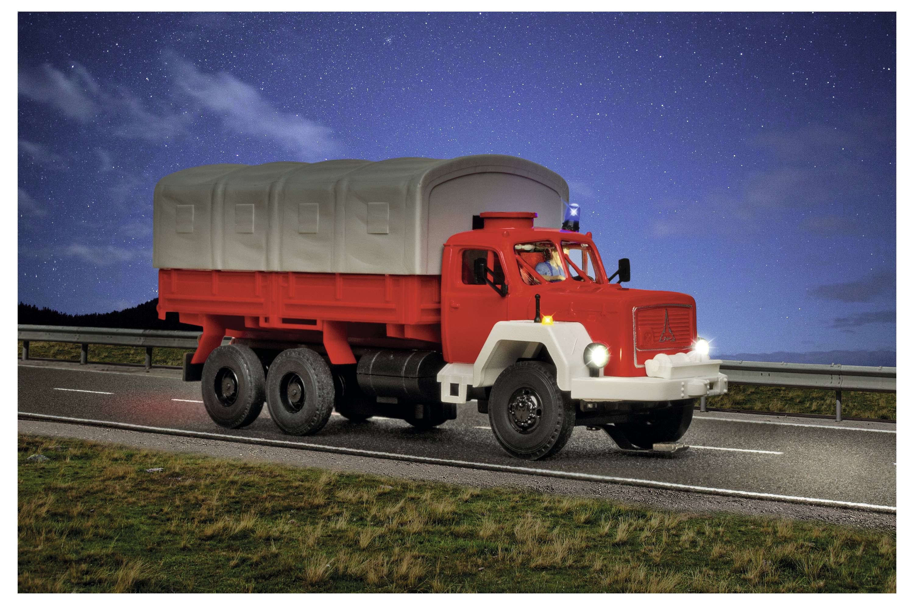Camion rosso e bianco da carico con un carico coperto che viaggia su un'autostrada di notte sotto un cielo stellato.