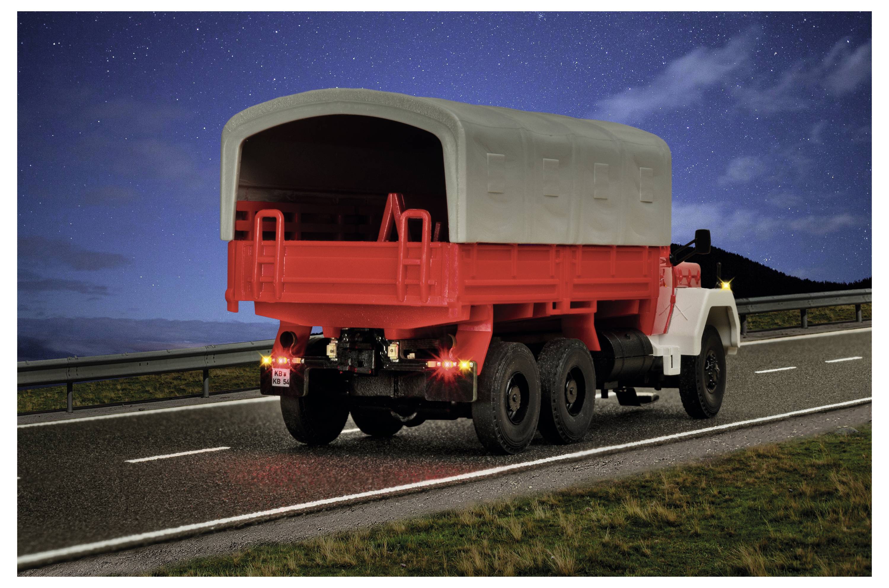 Vista posteriore di un camion rosso da carico con un cassone grigio coperto che guida su una strada di notte sotto un cielo stellato.