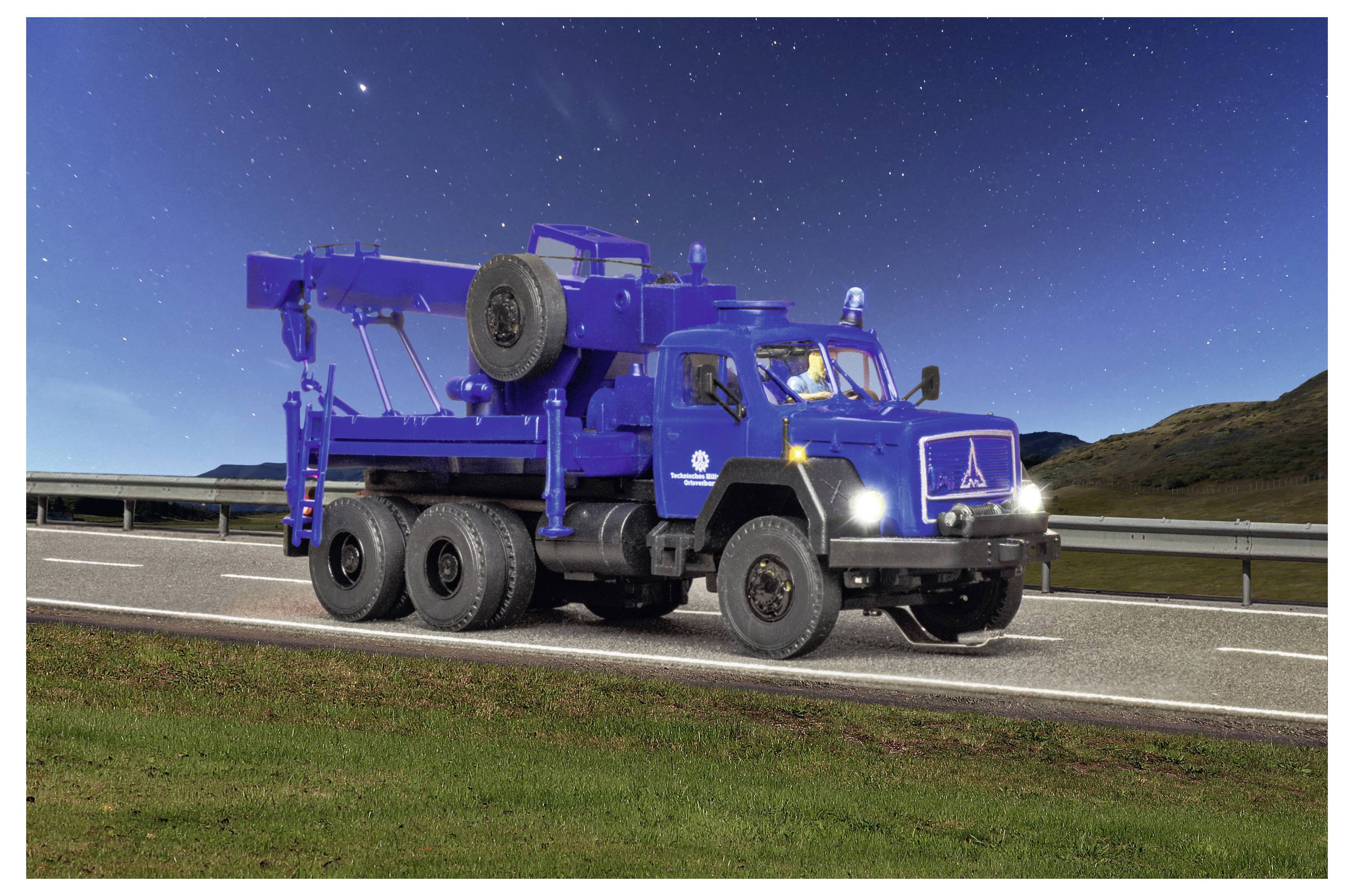 Camion blu per lavori pesanti parcheggiato a bordo strada di notte, con attrezzature montate e una ruota di scorta sul fianco sotto un cielo stellato.