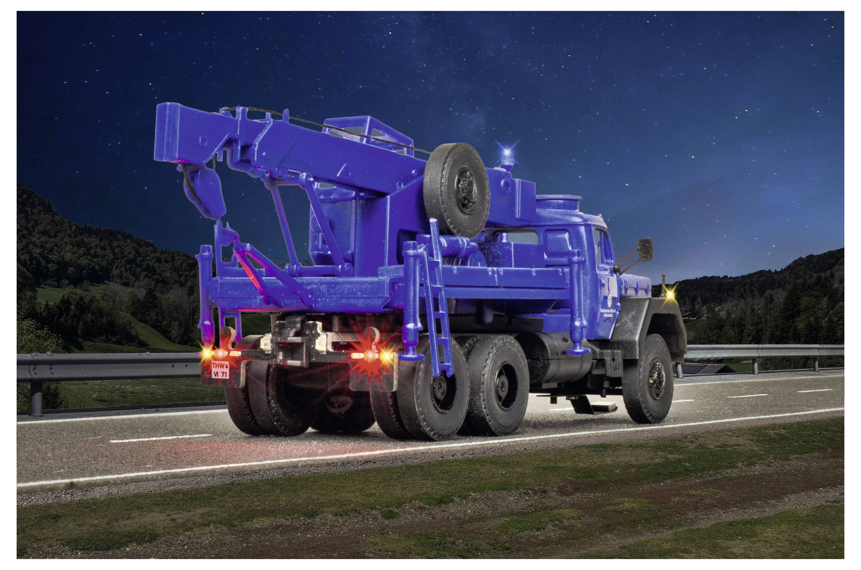 Camion carro attrezzi blu parcheggiato sul bordo della strada di notte con luci posteriori accese, ripreso da dietro su una strada statale rurale.