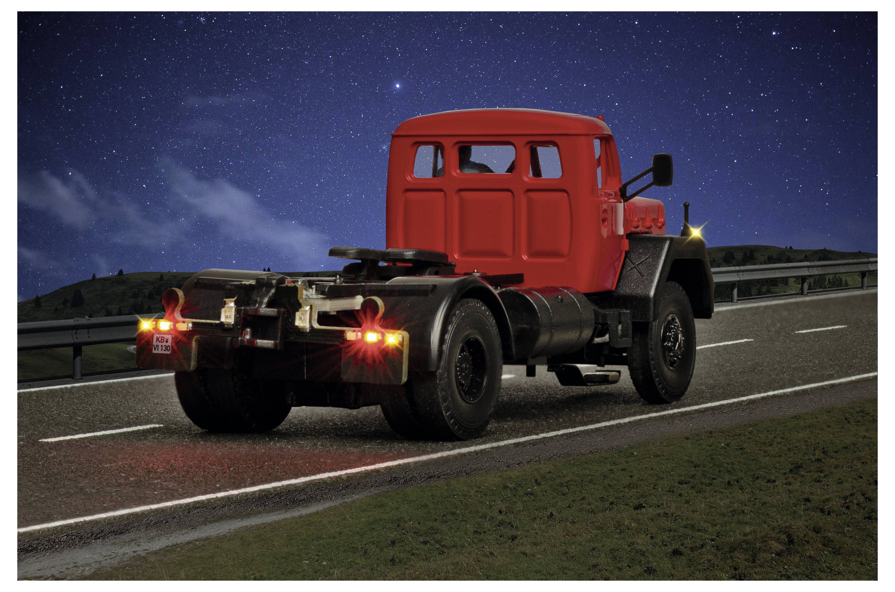Telaio di un autocarro cabinato rosso che percorre un'autostrada di notte, con le luci posteriori che brillano sotto un cielo stellato.
