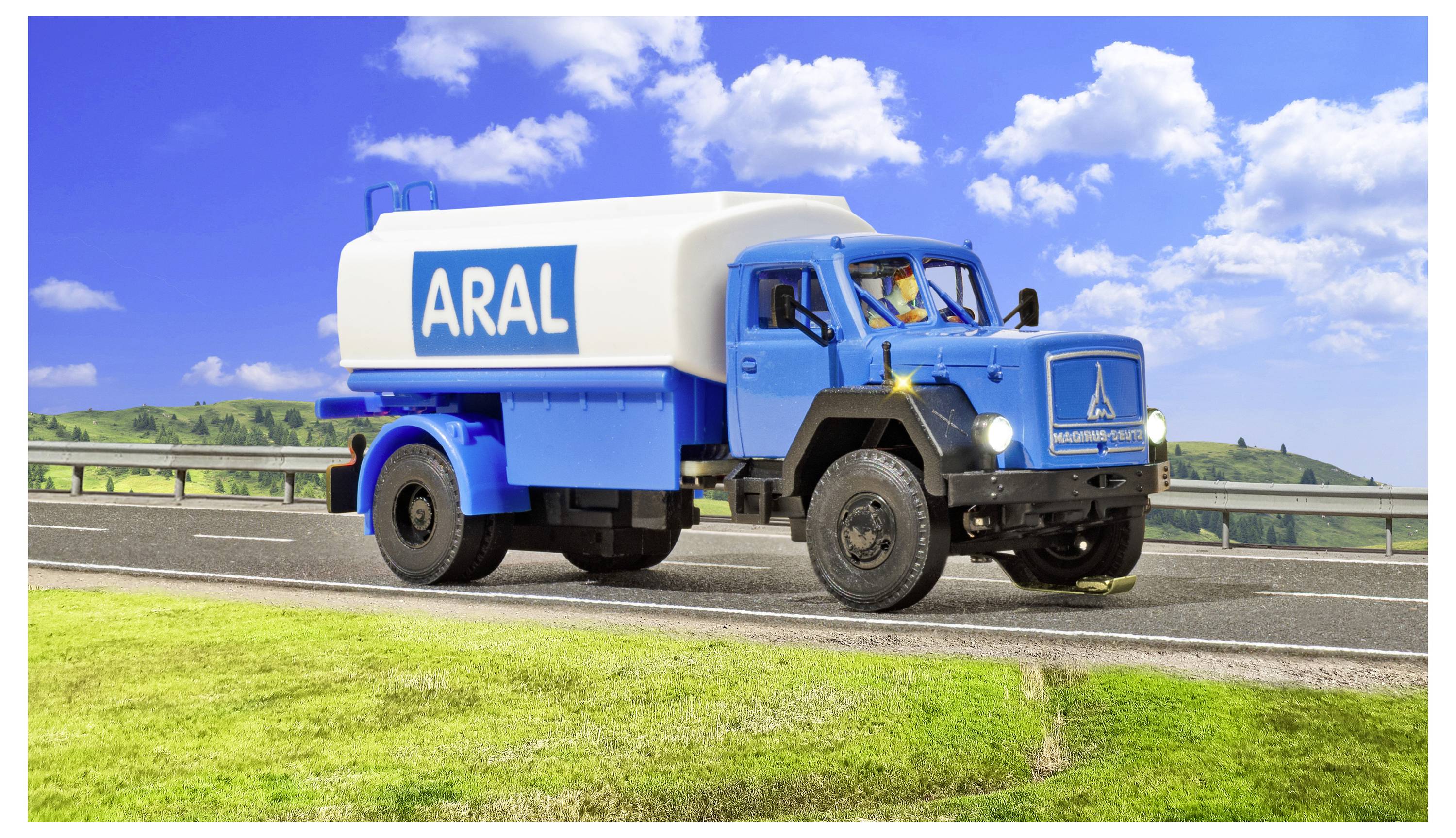 Autobotte di carburante ARAL blu che guida su una strada sotto un cielo azzurro luminoso con nuvole.