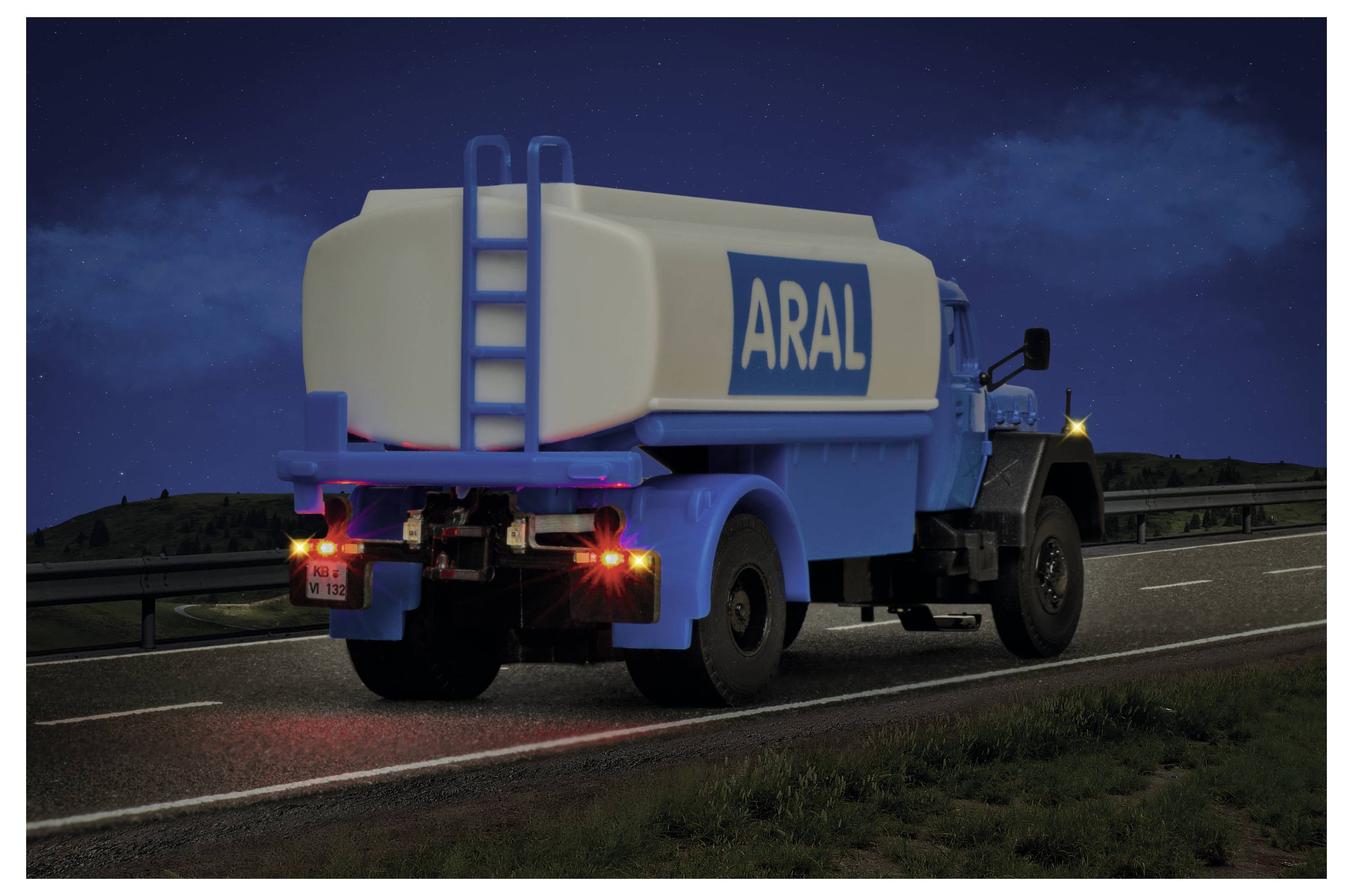 Autocisterna ARAL bianca e blu che guida su un'autostrada di notte con le luci posteriori accese.