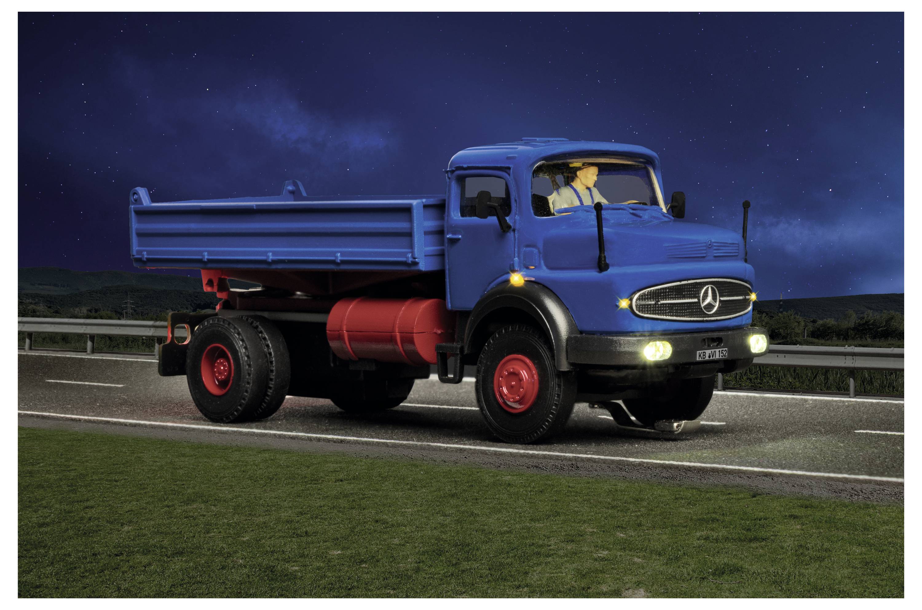 Camion ribaltabile Mercedes blu che guida su una strada di notte, fari accesi, con il conducente visibile nella cabina.