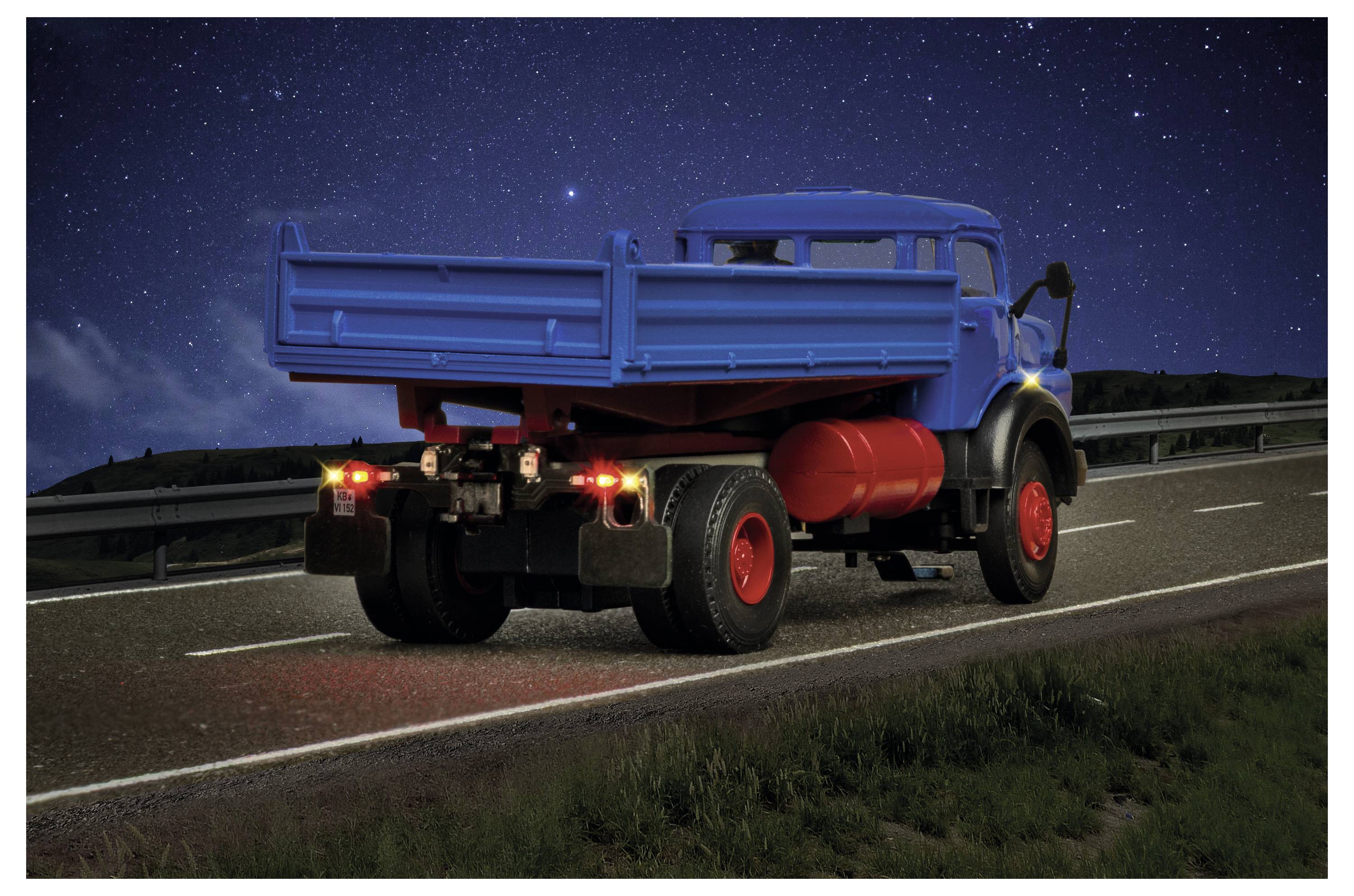 Camion ribaltabile blu che guida su un'autostrada di notte, visto da dietro con i fanali posteriori che brillano sotto un cielo stellato.