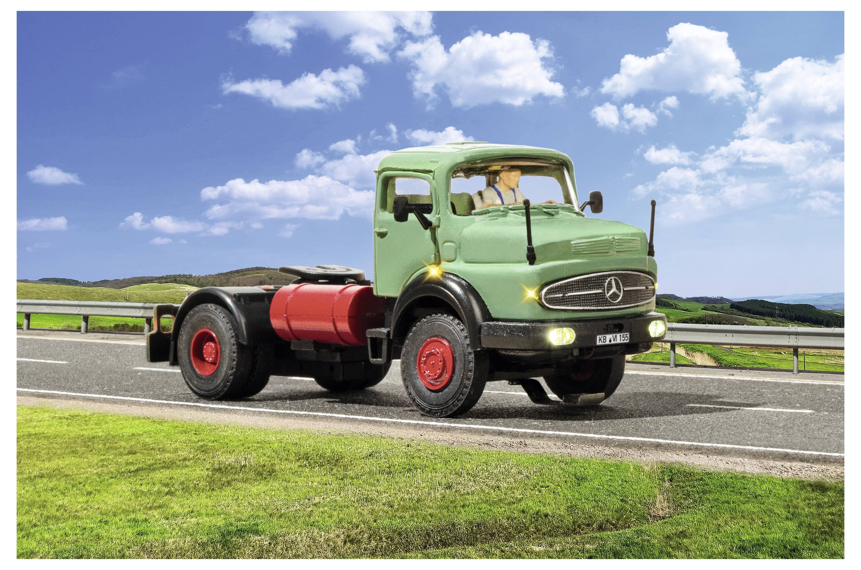 Un vintage camion Mercedes verde che guida su una strada rurale, mostrato in vista laterale con ruote rosse e serbatoio del carburante sotto un cielo blu.