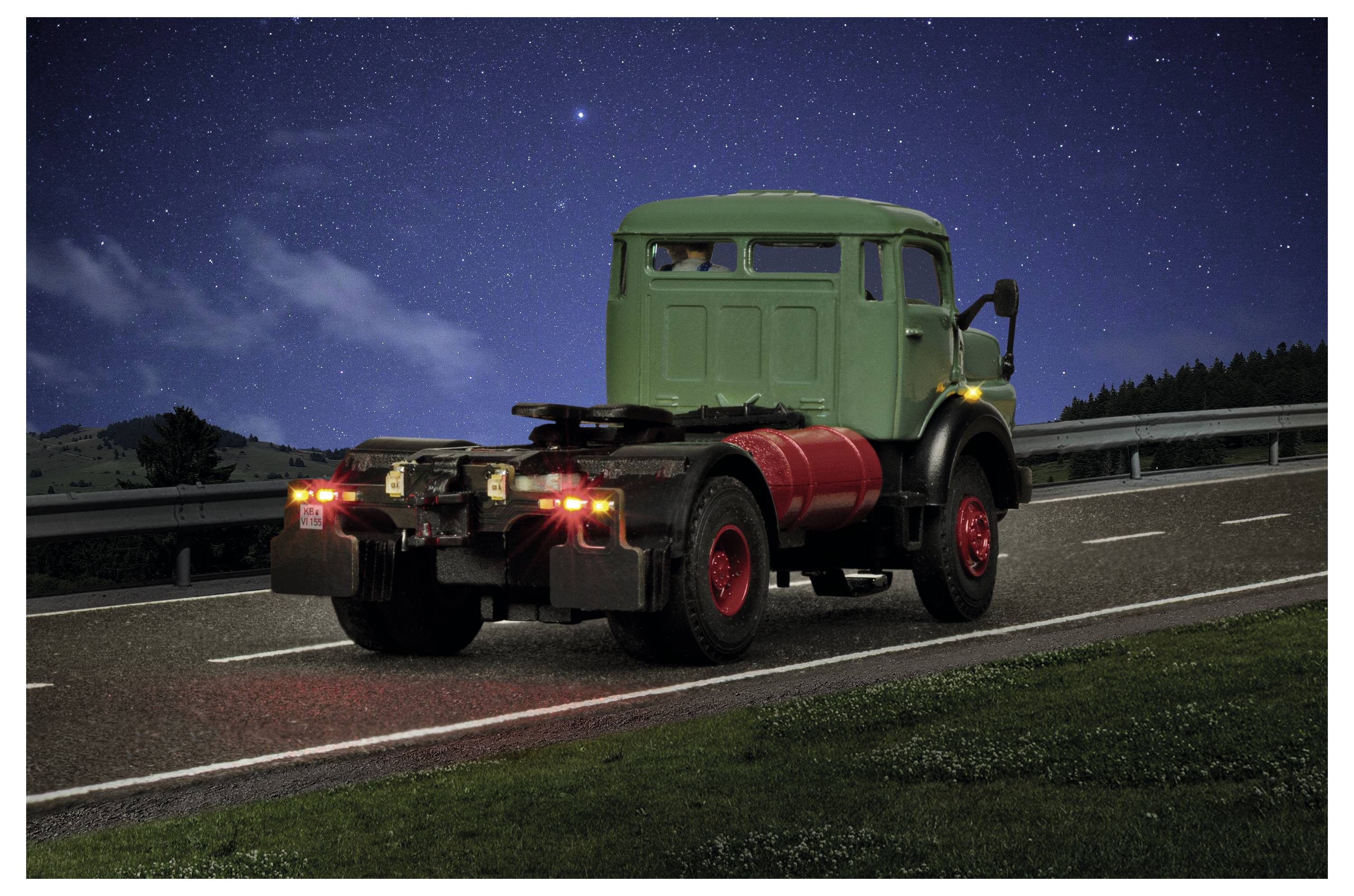 Camion vintage verde che guida di notte su un'autostrada sotto un cielo stellato, con le luci rosse di coda visibili.