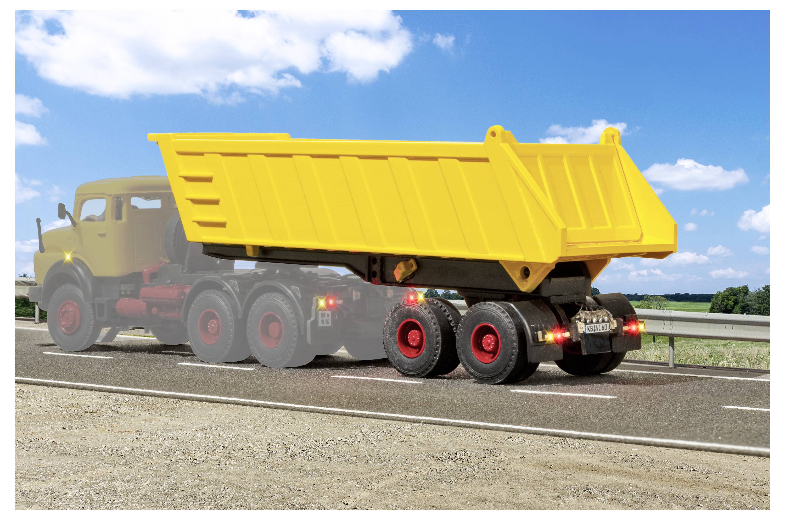 Camion ribaltabile giallo con cassone sollevato parcheggiato sulla spalla di un'autostrada sotto un cielo blu.