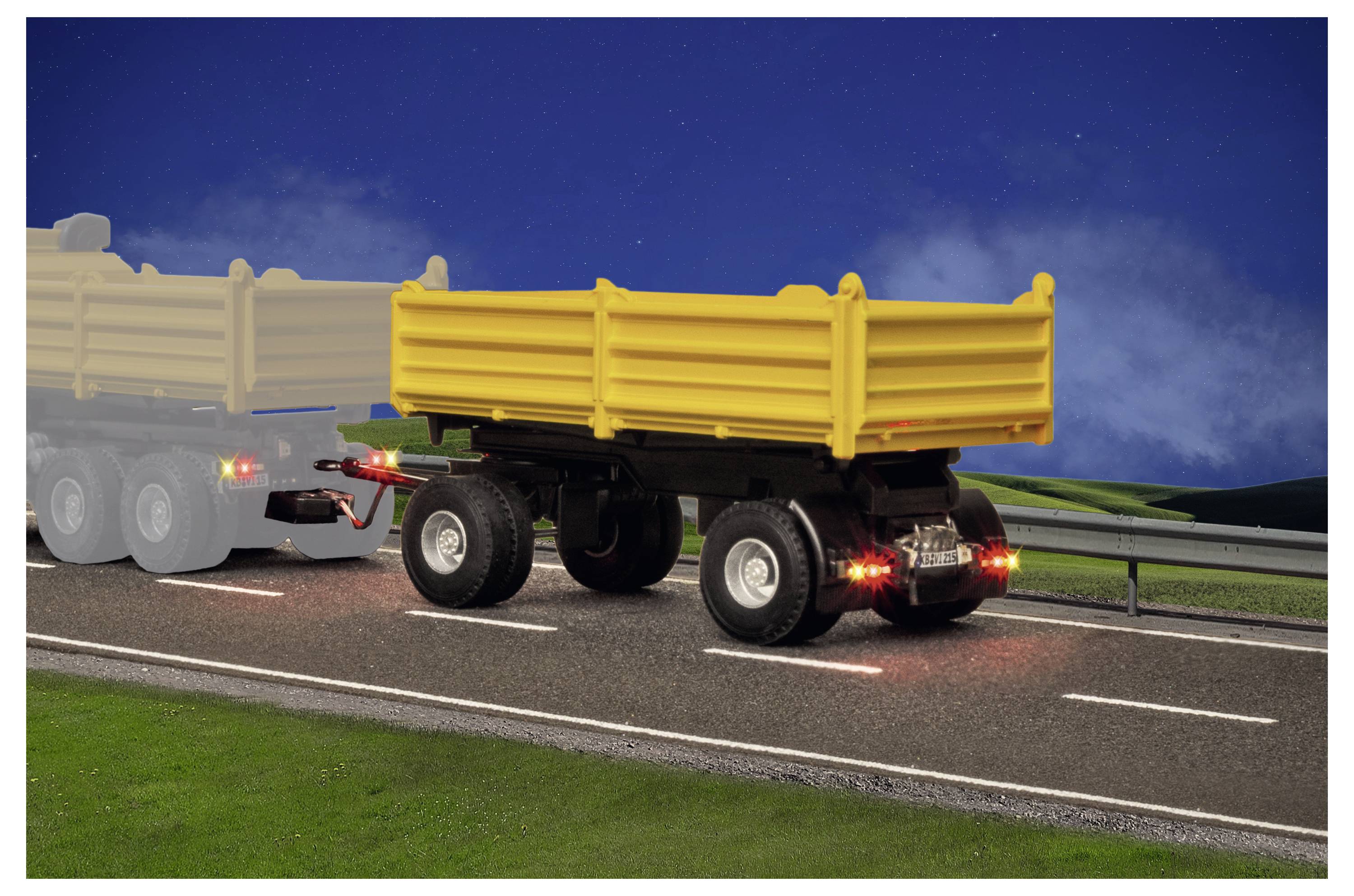 Rimorchio scarico giallo trascinato su un'autostrada di notte, con luci rosse posteriori visibili e un camion sbiadito davanti sullo sfondo.