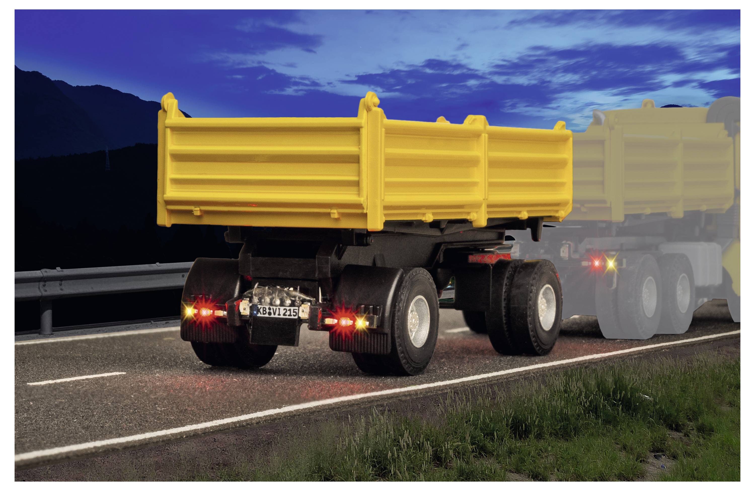 Camion ribaltabile giallo che guida al crepuscolo su una strada rurale, con un altro camion che svanisce sullo sfondo.