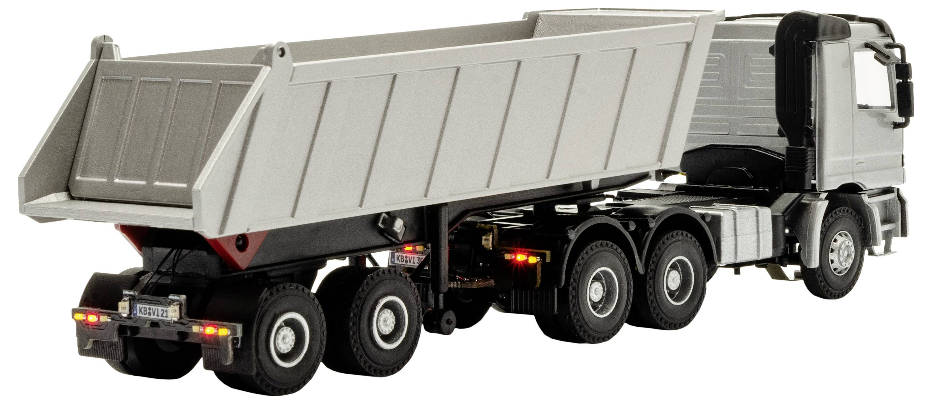 Vista laterale di un camion ribaltabile bianco con il cassone posteriore sollevato, che mostra il meccanismo di ribaltamento e i multipli assi posteriori.