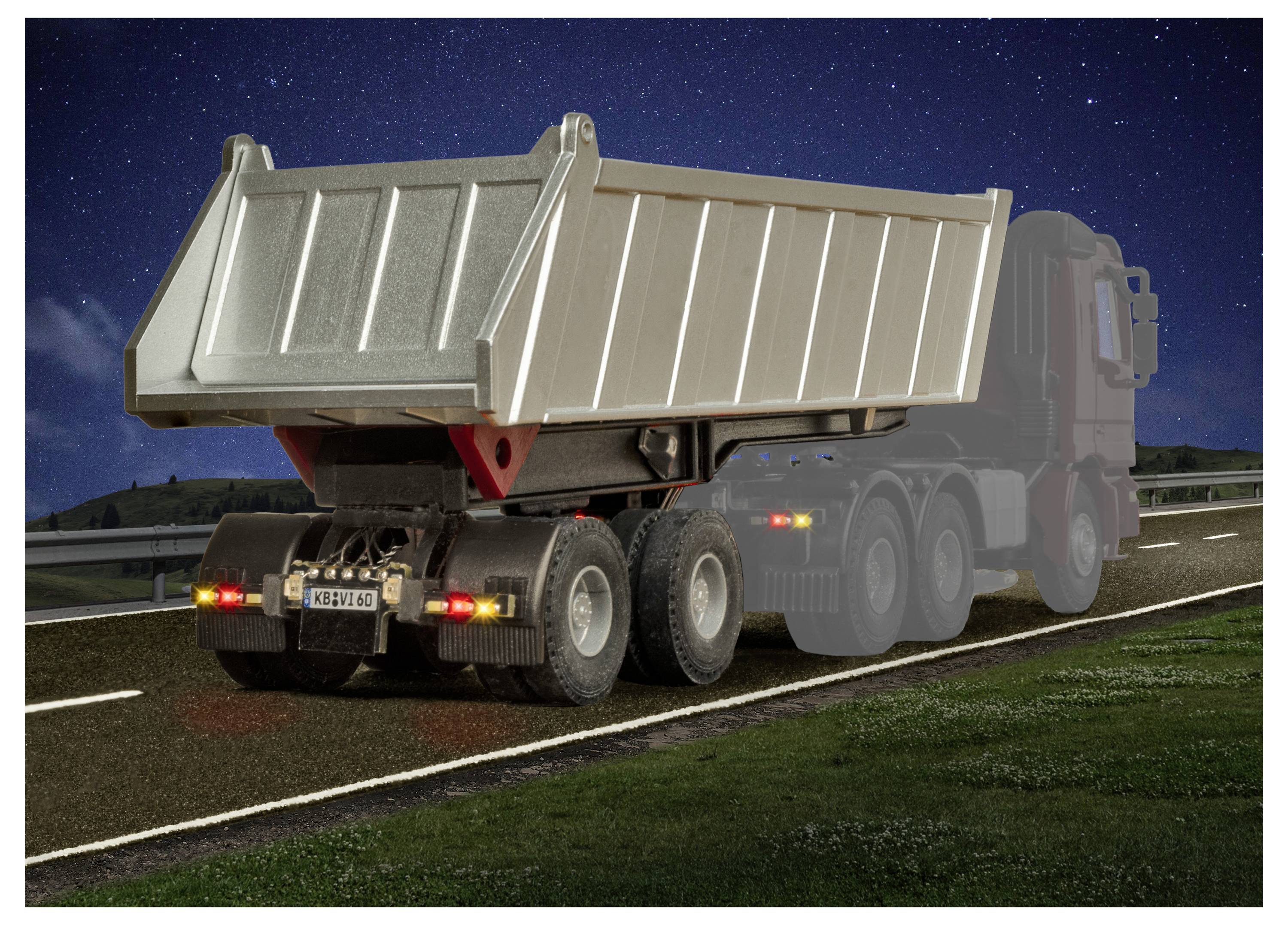 Vista posteriore di un grande camion ribaltabile che guida su una strada di notte, con fanali rossi posteriori e un cassone metallico di carico sollevato.