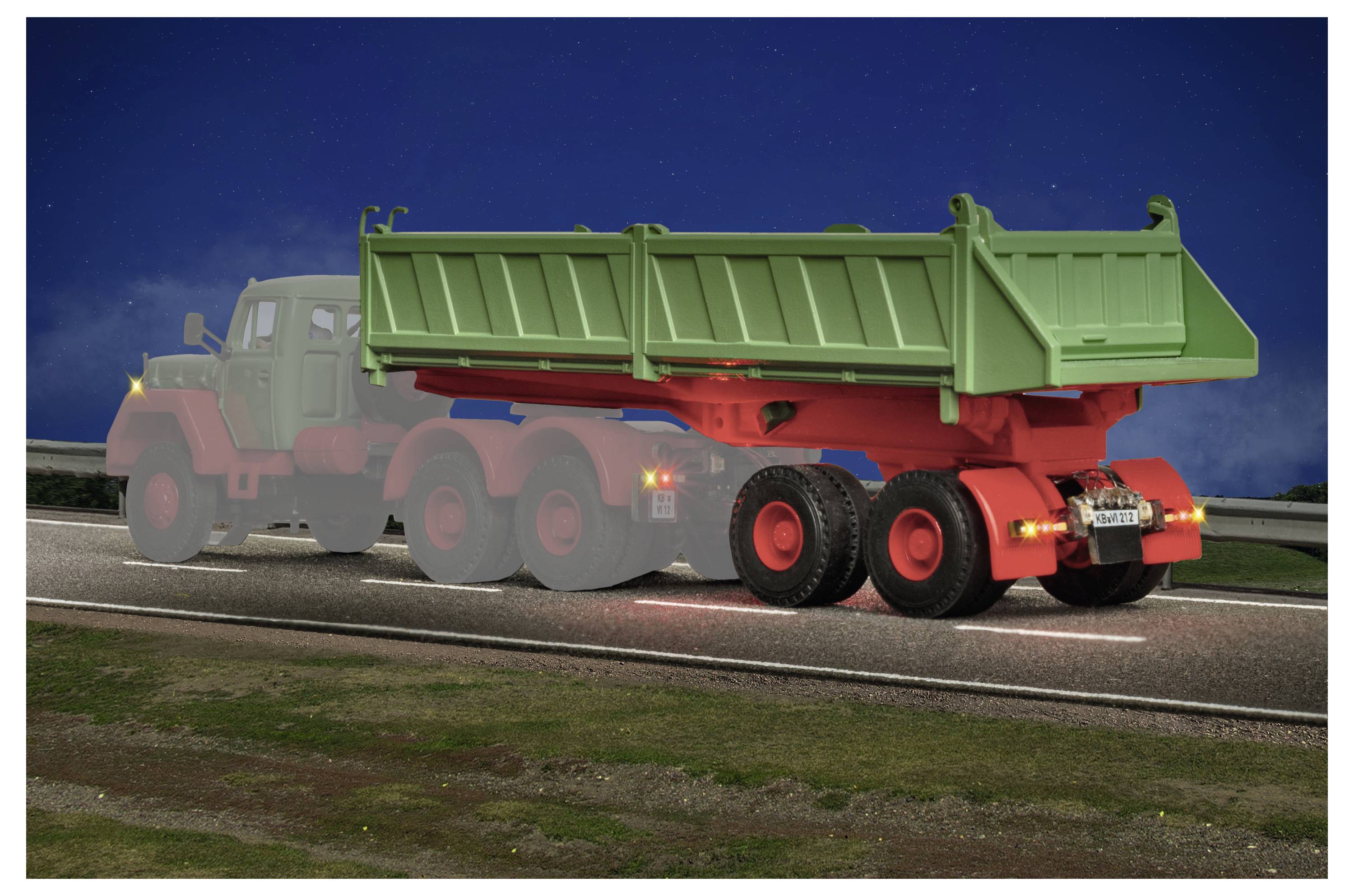 Un pesante camion ribaltabile con un cassone di carico verde guida su una strada di notte, mostrato con una debole traccia di movimento.