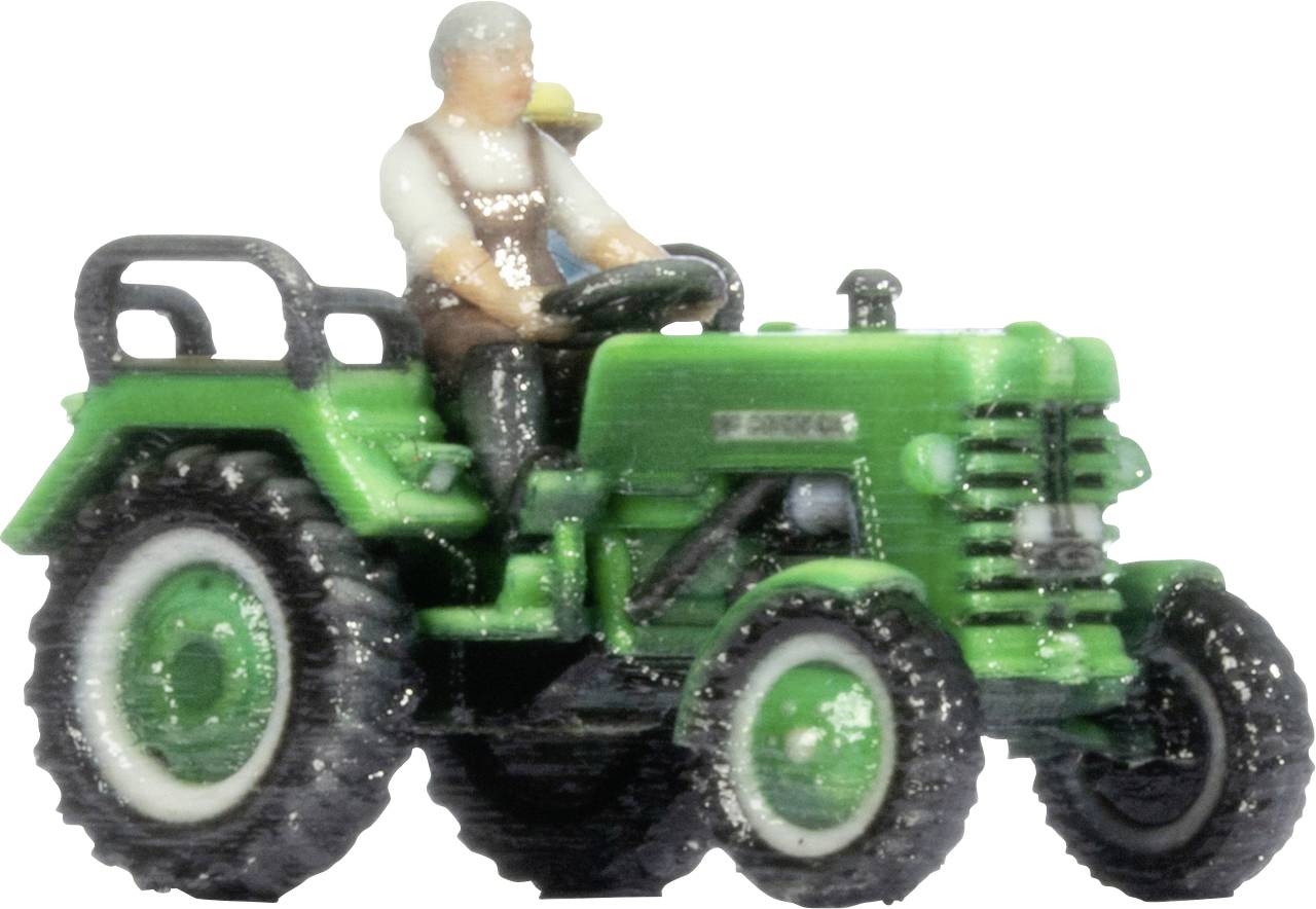 Trattore giocattolo verde con un piccolo autista seduto, mostrato in vista laterale su uno sfondo neutro.